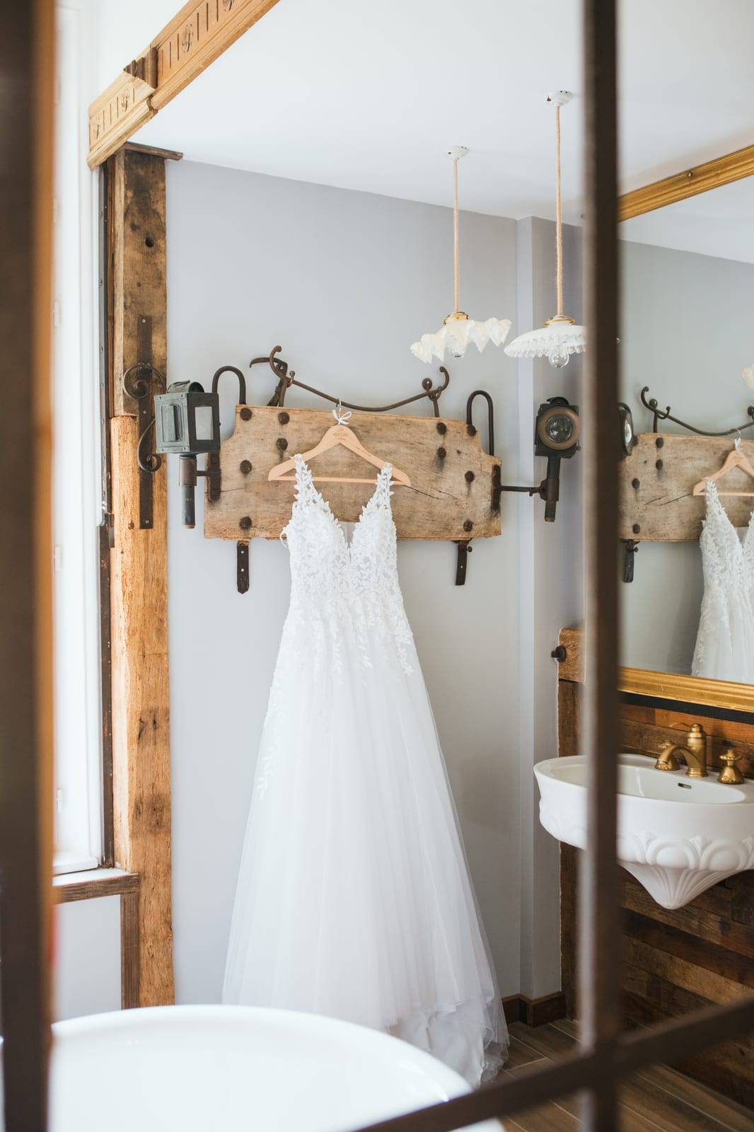 La robe de mariée en dentelle et tulle suspendue à une patère ancienne, reflétée dans le miroir de la salle d'eau du domaine, mariage au Domaine de Senercy, par Jean-Baptiste Argyre (Jaysphotography)