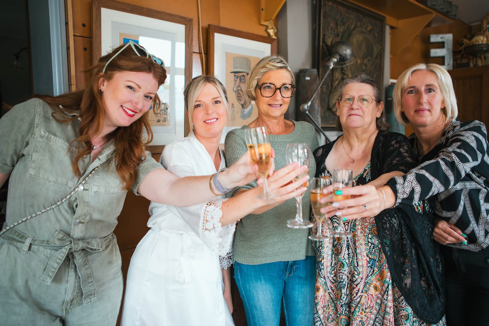 Amandine et ses proches trinquent au champagne pendant les préparatifs, dans une pièce ornée de tableaux, mariage au Domaine de Senercy, par Jean-Baptiste Argyre (Jaysphotography)