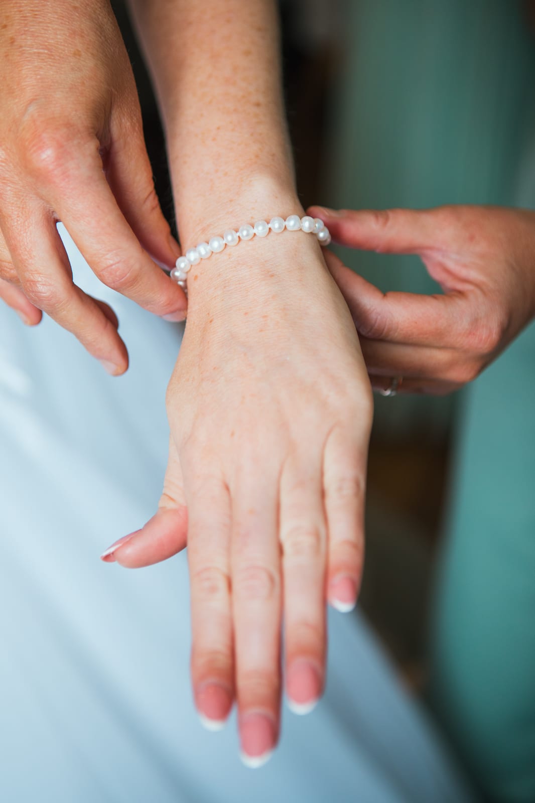 Gros plan sur la pose d'un bracelet de perles au poignet d'Amandine pendant l'habillage de la mariée, mariage au Domaine de Senercy, par Jean-Baptiste Argyre (Jaysphotography)