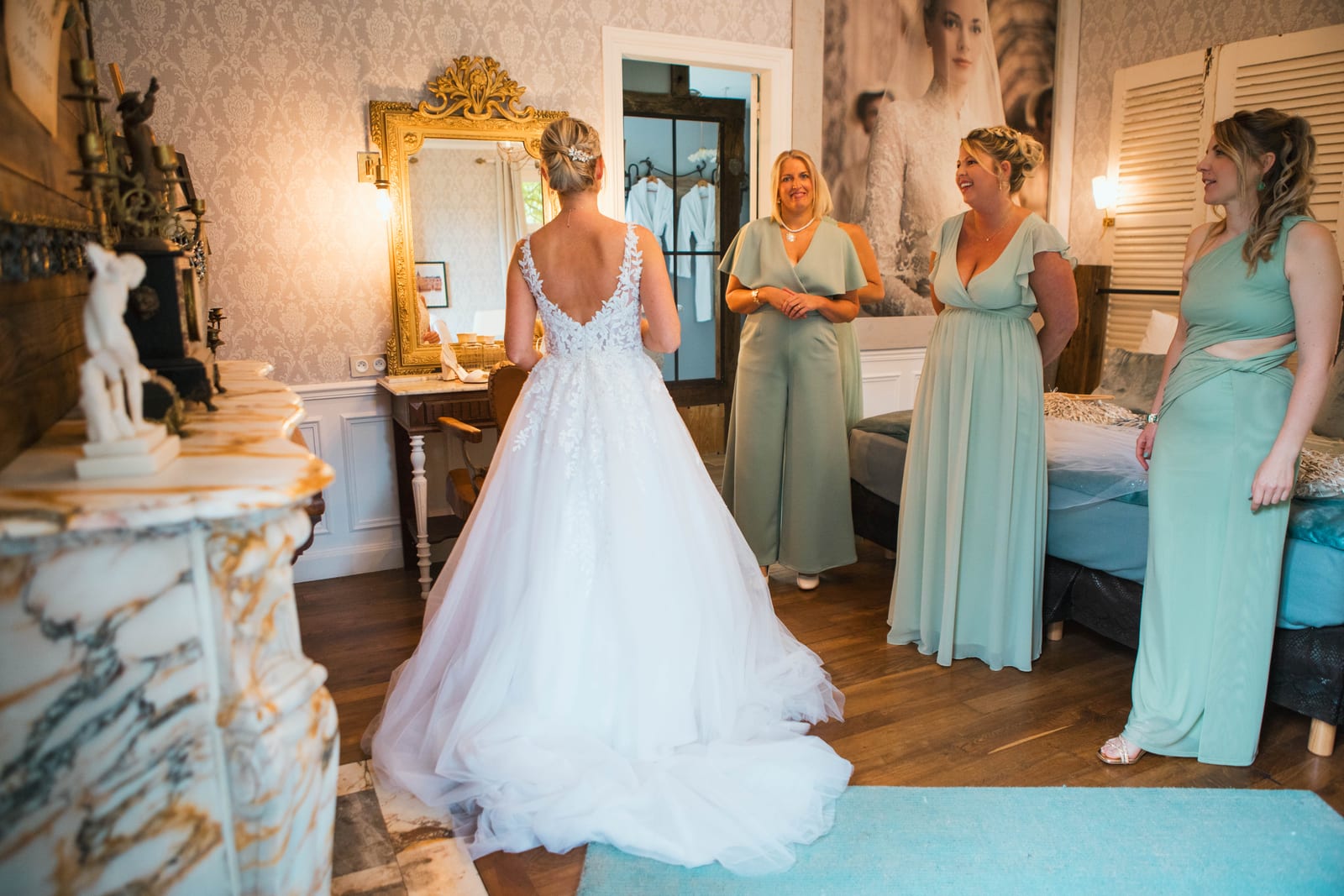 Amandine de dos en robe de mariée à dos décolleté découvre sa tenue à ses demoiselles d'honneur dans la pièce des préparatifs, mariage au Domaine de Senercy, par Jean-Baptiste Argyre (Jaysphotography)