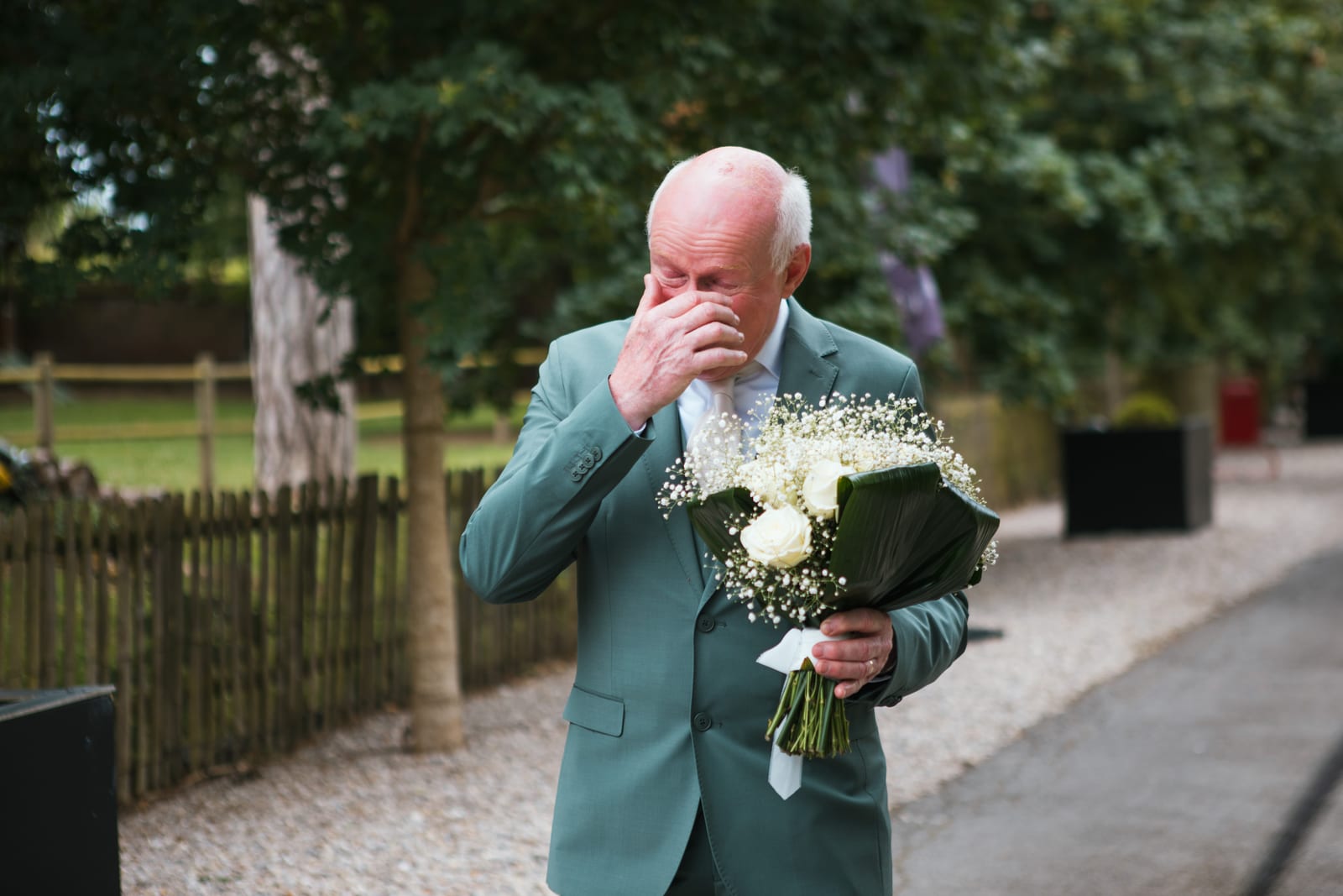 Le papa d'Amandine, ému aux larmes, tient le bouquet de roses blanches et de gypsophile lors du first look avec sa fille, mariage au Domaine de Senercy, par Jean-Baptiste Argyre (Jaysphotography)