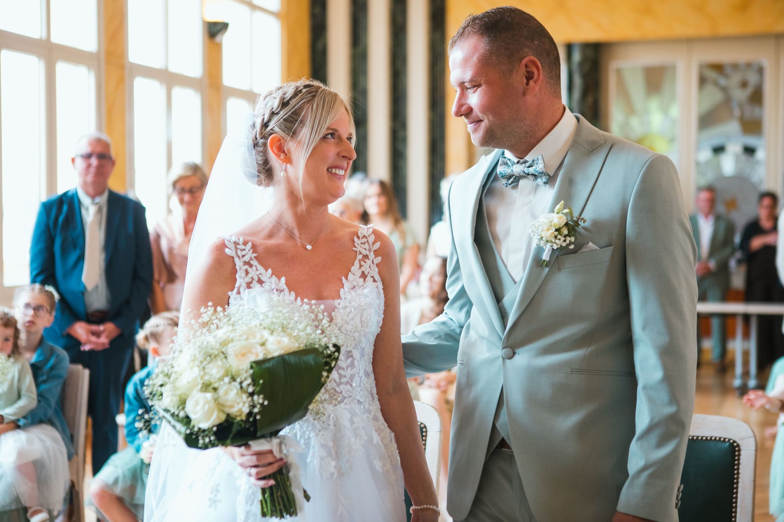 Amandine et Benjamin se font face en souriant à leur entrée dans la salle lumineuse de la mairie, mariage au Domaine de Senercy, par Jean-Baptiste Argyre (Jaysphotography)