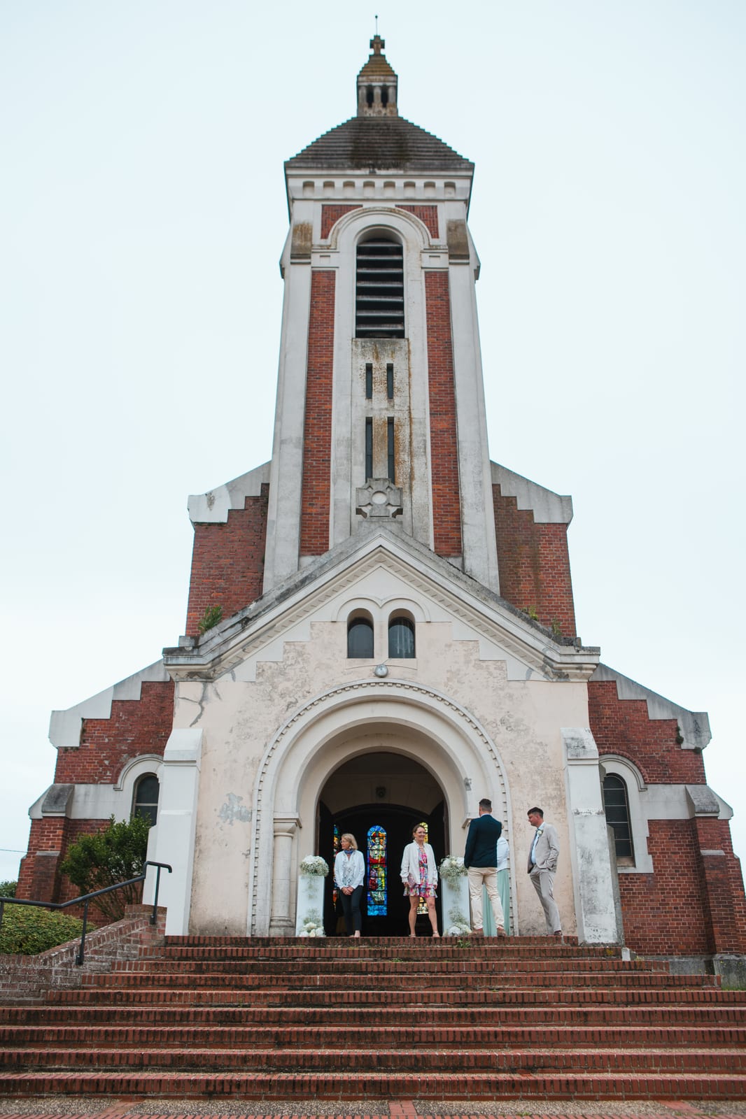 Façade en brique et pierre de l'église de Tergnier et son haut clocher carré, vue en contre-plongée depuis le perron, mariage au Domaine de Senercy, par Jean-Baptiste Argyre (Jaysphotography)