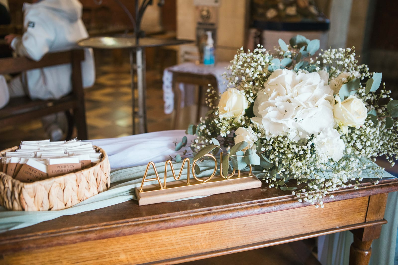 Décoration de l'église : lettres dorées "Amour", panier de livrets et bouquet d'hortensias et de gypsophile blancs, mariage au Domaine de Senercy, par Jean-Baptiste Argyre (Jaysphotography)