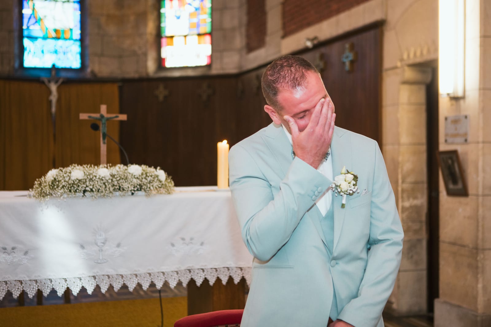 Benjamin, ému, essuie une larme devant l'autel fleuri de l'église de Tergnier avant l'entrée de la mariée, mariage au Domaine de Senercy, par Jean-Baptiste Argyre (Jaysphotography)