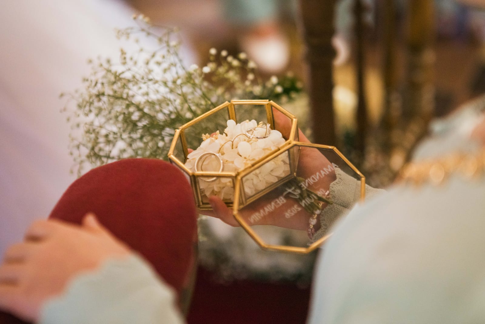 Détail des alliances dans leur écrin hexagonal en verre garni de pétales blancs, tenu pendant la cérémonie religieuse, mariage au Domaine de Senercy, par Jean-Baptiste Argyre (Jaysphotography)