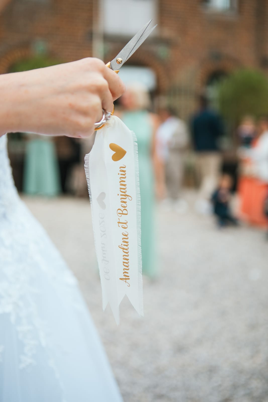 Amandine tient les ciseaux dorés et un ruban personnalisé "Amandine et Benjamin" lors de la ronde des rubans, mariage au Domaine de Senercy, par Jean-Baptiste Argyre (Jaysphotography)