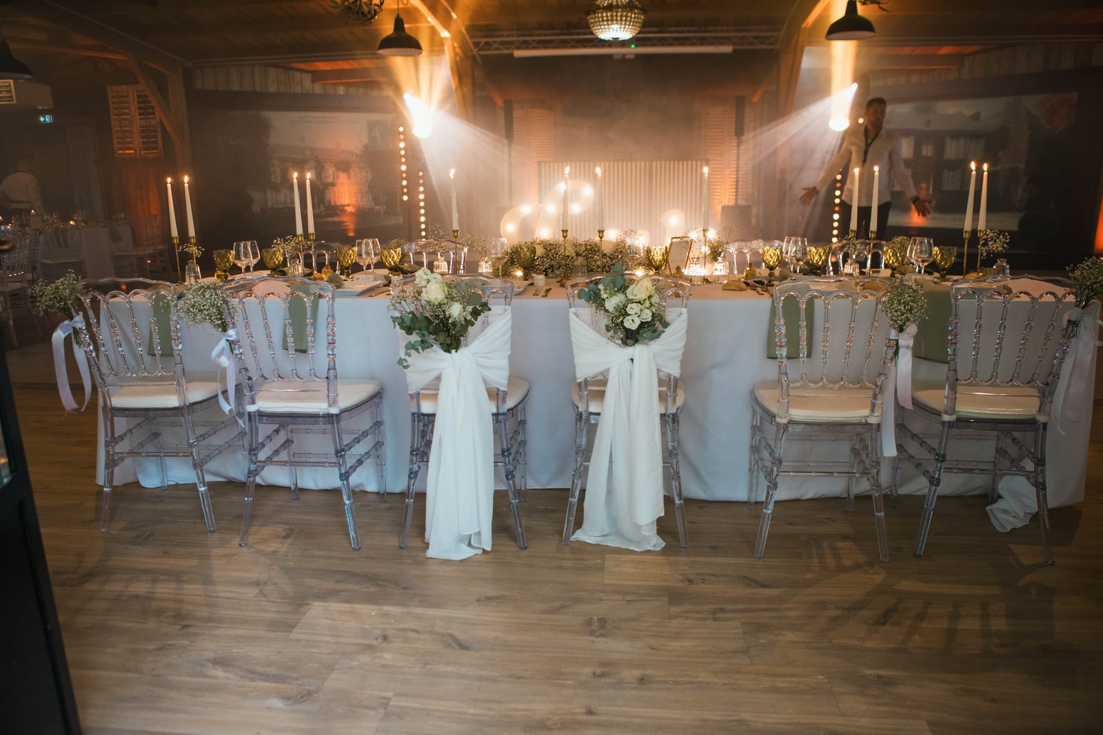 La table d'honneur dressée : chaises transparentes, chemins d'eucalyptus, chandeliers et drapés blancs noués sur les chaises des mariés, mariage au Domaine de Senercy, par Jean-Baptiste Argyre (Jaysphotography)