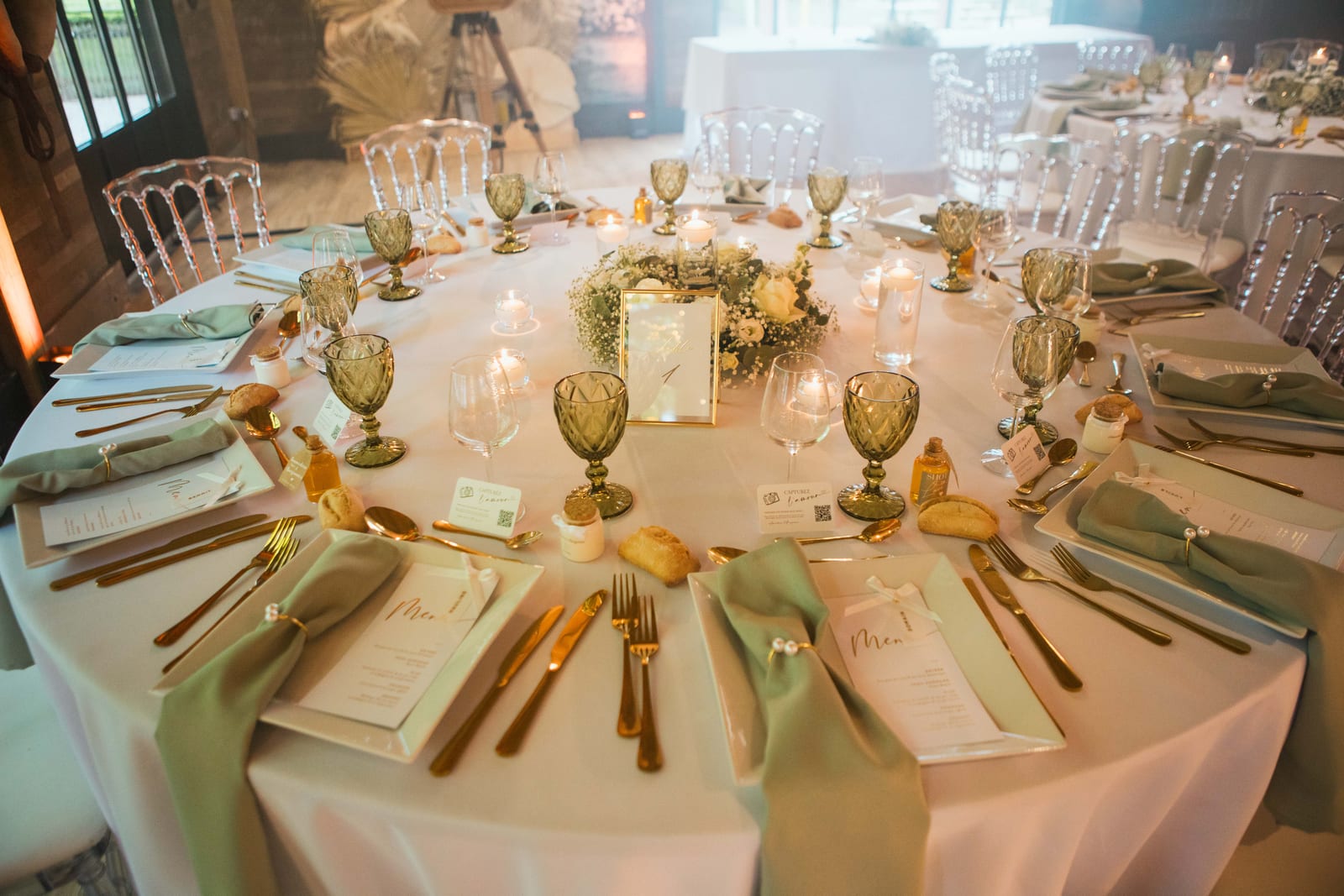 Table ronde dressée aux serviettes vert sauge, couverts dorés, verres en cristal vert et centre de gypsophile, mariage au Domaine de Senercy, par Jean-Baptiste Argyre (Jaysphotography)