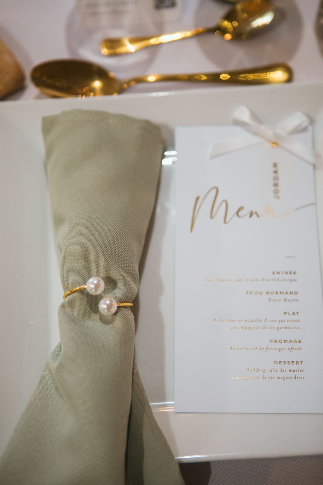 Détail d'un couvert : serviette vert sauge à l'anneau de perles et menu doré du dîner de mariage, mariage au Domaine de Senercy, par Jean-Baptiste Argyre (Jaysphotography)