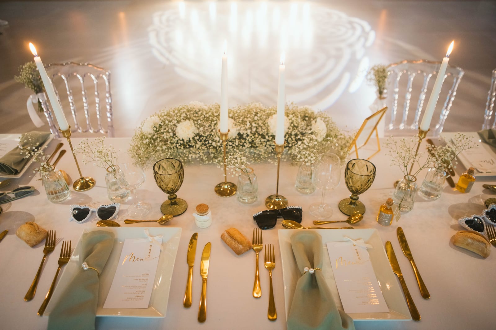 La table d'honneur des mariés vue de face, gobo lumineux projeté au mur, centre de gypsophile et lunettes en cœur, mariage au Domaine de Senercy, par Jean-Baptiste Argyre (Jaysphotography)