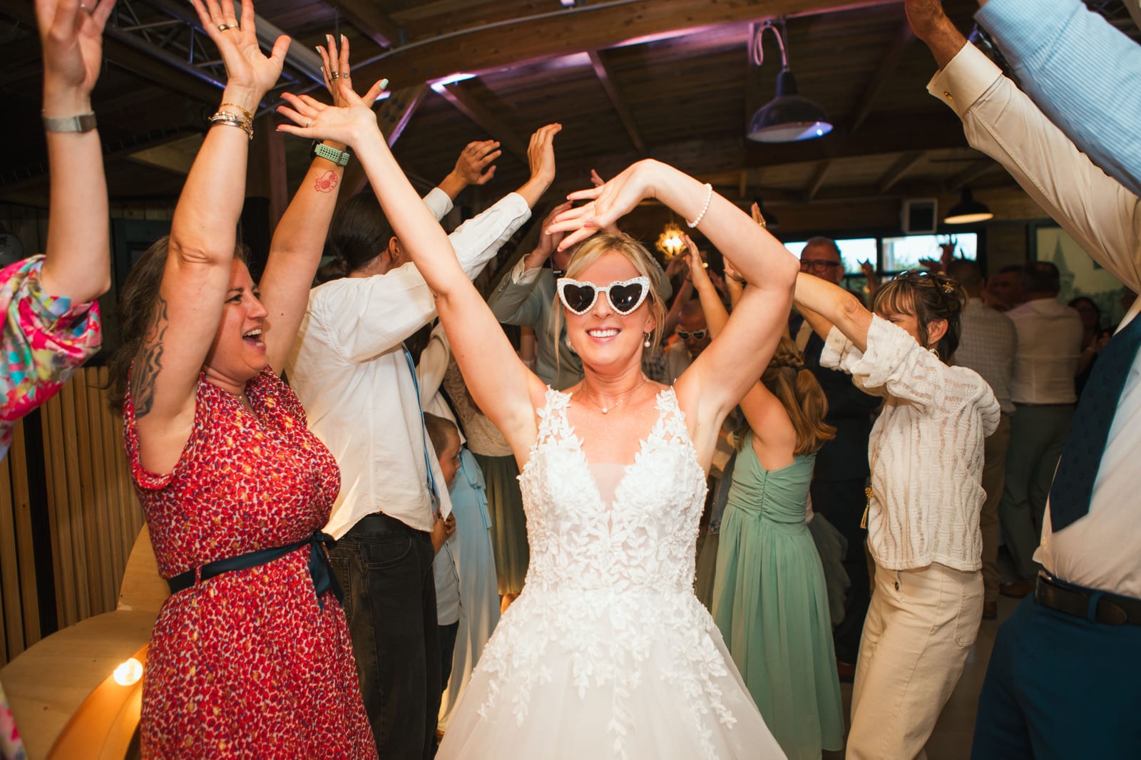 Amandine, lunettes en cœur, lève les bras au milieu de la piste de danse pendant la soirée, mariage au Domaine de Senercy, par Jean-Baptiste Argyre (Jaysphotography)