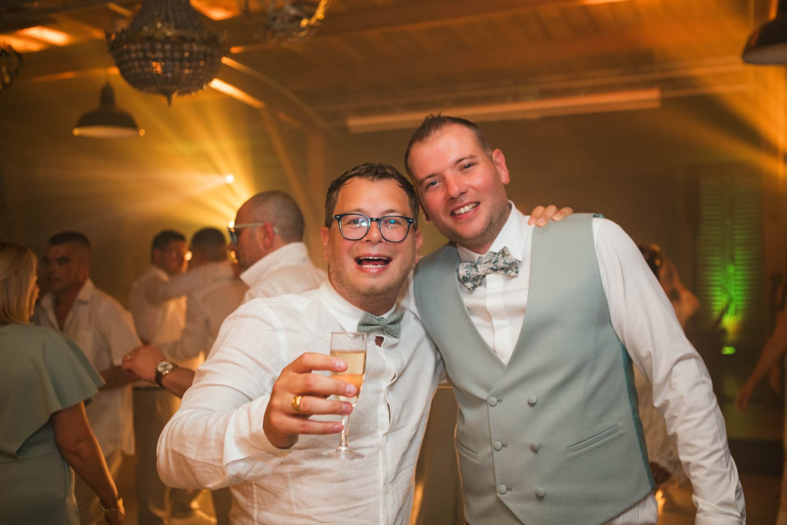 Benjamin trinque au champagne, joue contre joue avec un invité, dans la lumière chaude de la fête, mariage au Domaine de Senercy, par Jean-Baptiste Argyre (Jaysphotography)