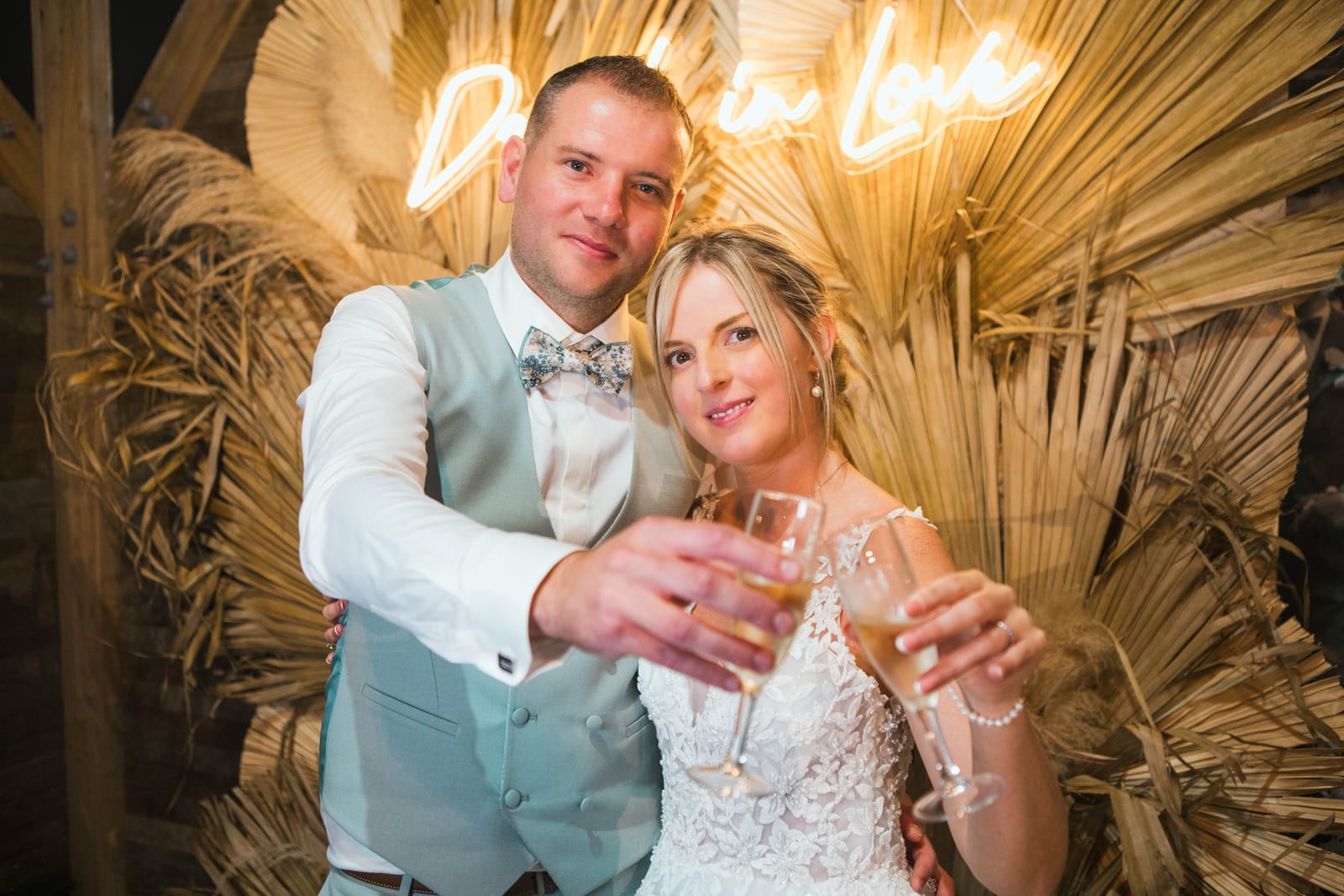 Amandine et Benjamin lèvent leur coupe de champagne au photo booth devant l'enseigne néon "Drunk in Love", mariage au Domaine de Senercy, par Jean-Baptiste Argyre (Jaysphotography)