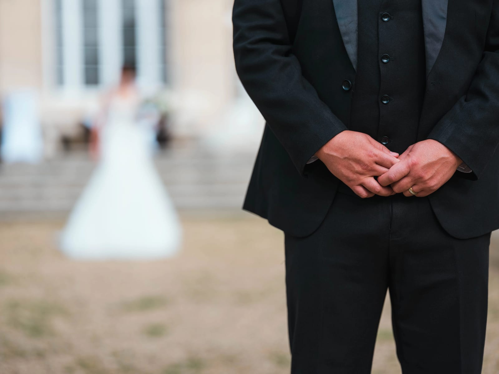 First look : le marié attend mains jointes au premier plan, la mariée floue arrive derrière lui depuis les marches de la façade, mariage au Château de Montvillargenne, Gouvieux, par Jean-Baptiste Argyre (Jaysphotography)
