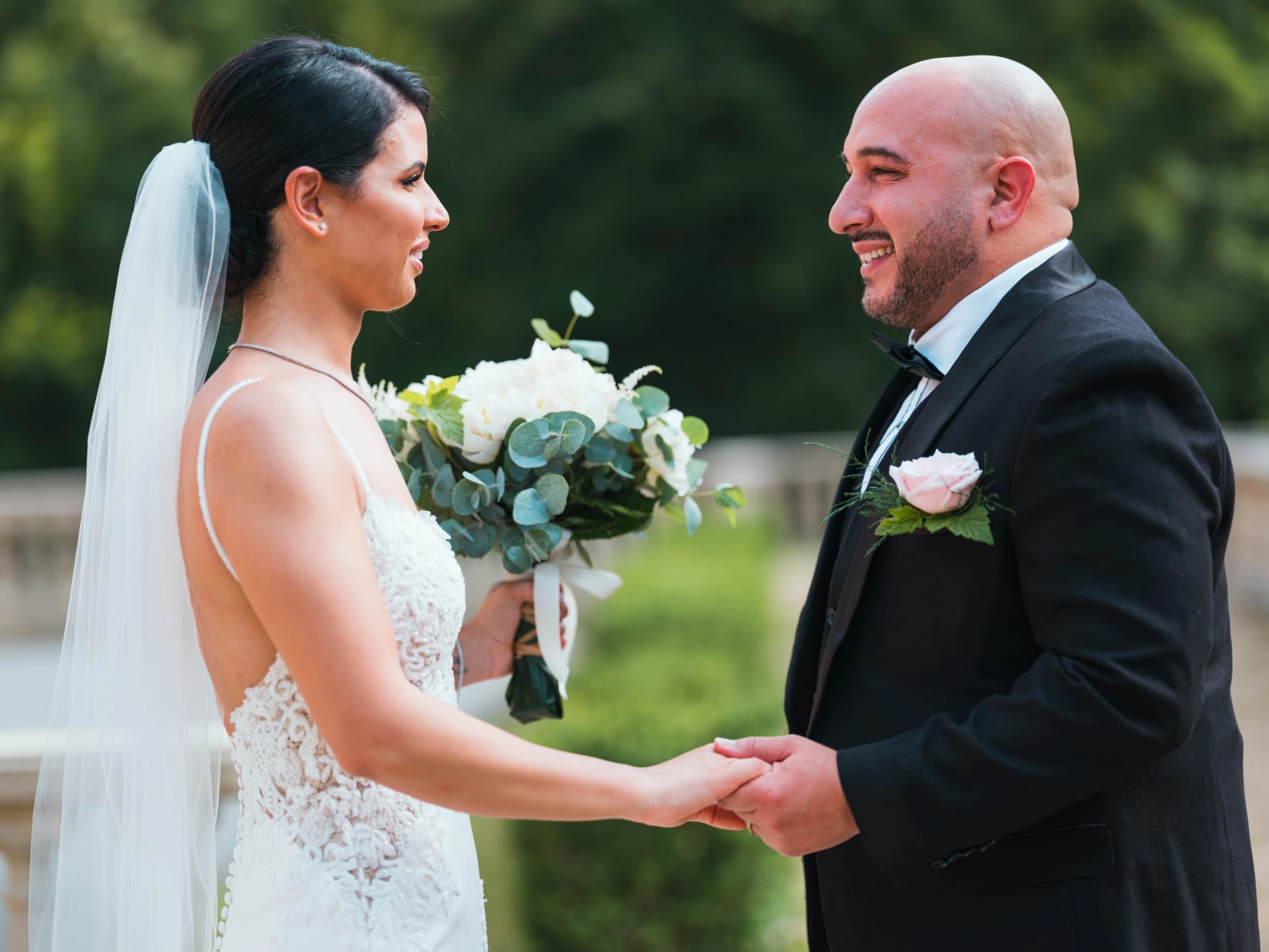 Les mariés face à face mains dans les mains au bord d'une balustrade, rose pâle à la boutonnière du marié, mariage au Château de Montvillargenne, Gouvieux, par Jean-Baptiste Argyre (Jaysphotography)