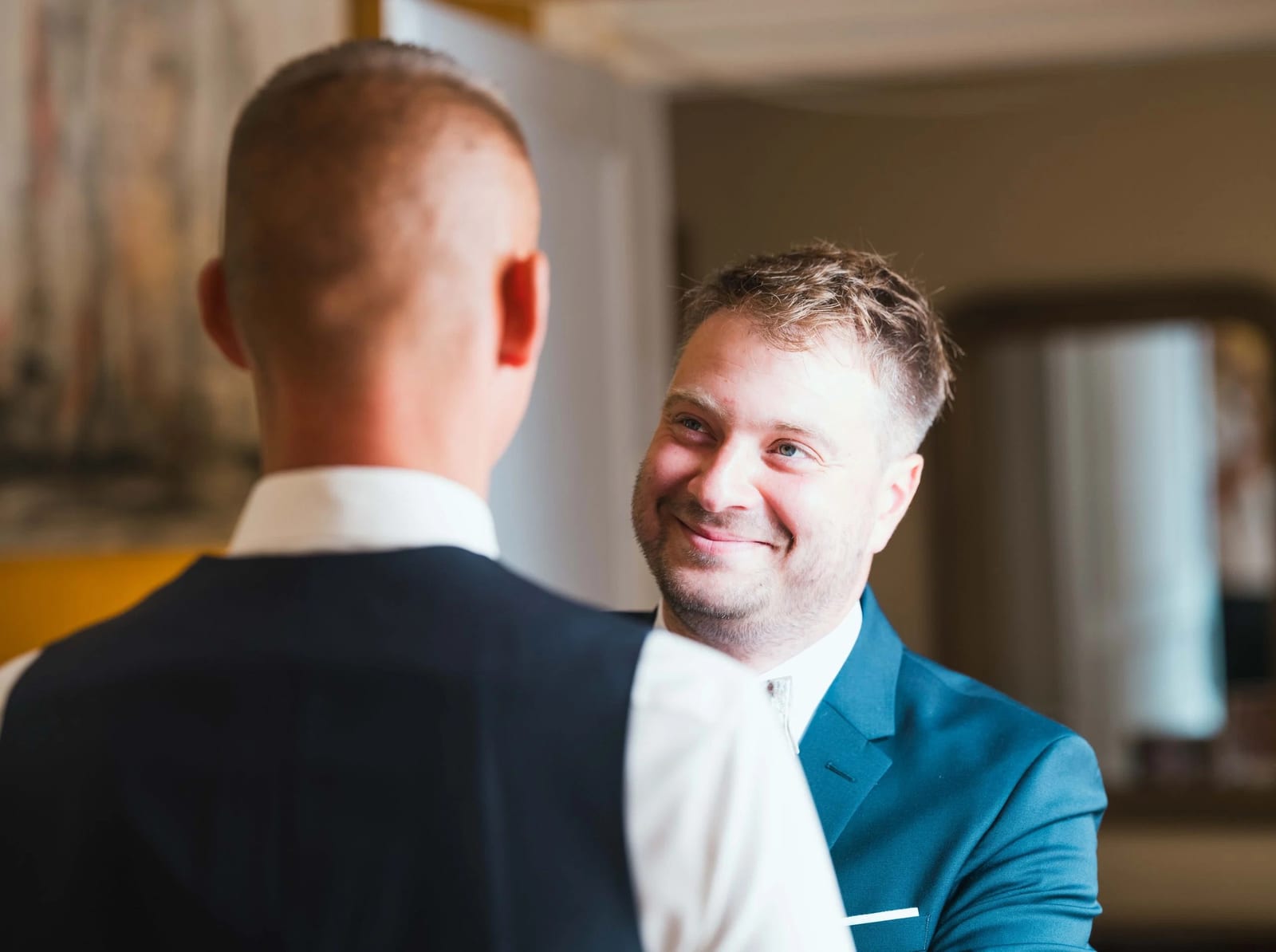 Guillaume ajuste sa veste bleu marine avec ses témoins dans un salon aux murs jaunes, éclat de rire, mariage au Les Voûtes du Plessier, par Jean-Baptiste Argyre (Jaysphotography)