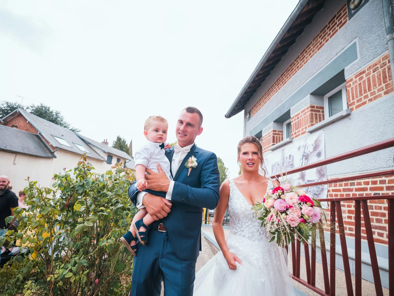 Amélie, Guillaume et leur fils sur la passerelle de brique rouge à la sortie de la mairie, mariage au Les Voûtes du Plessier, par Jean-Baptiste Argyre (Jaysphotography)