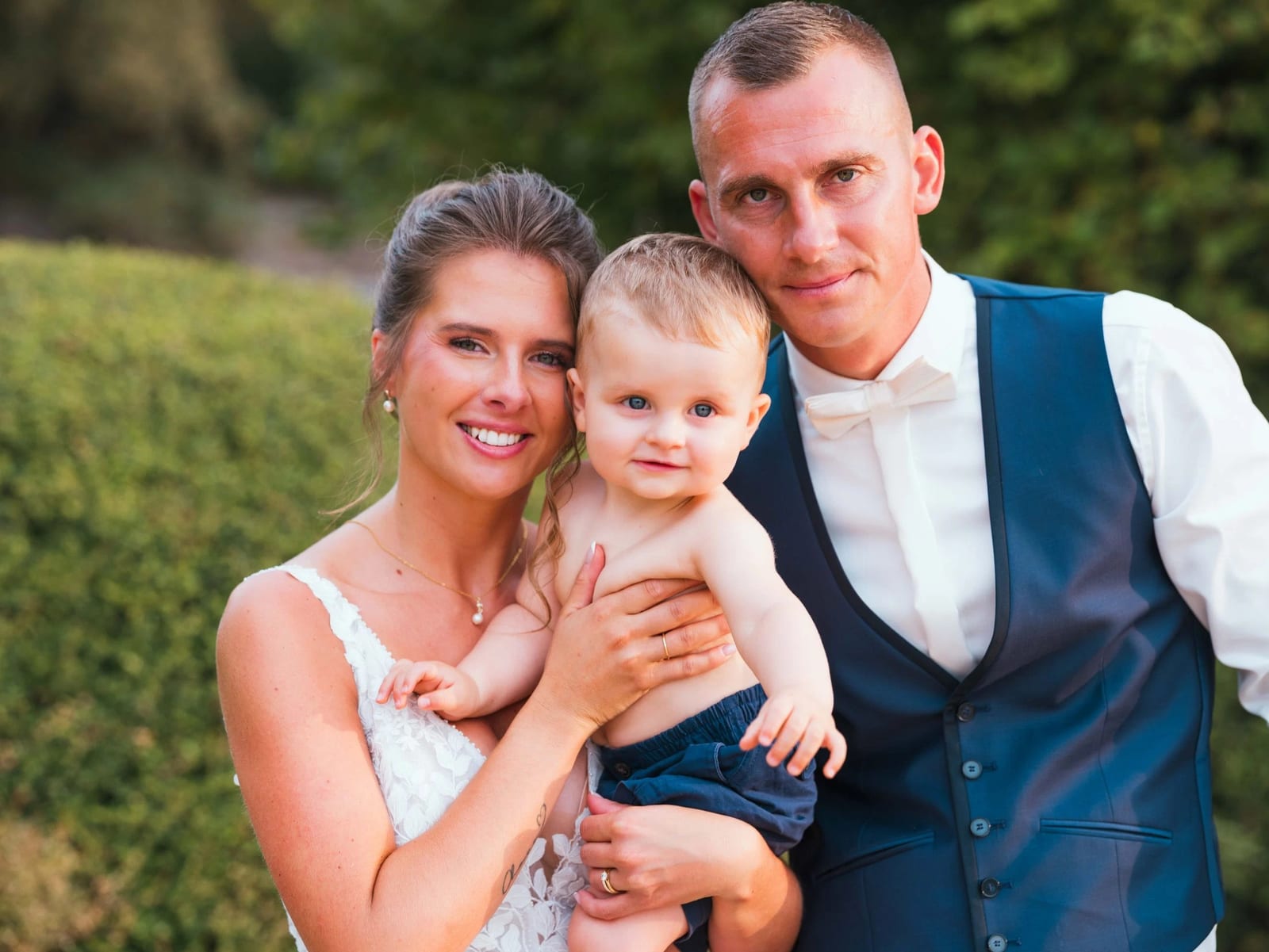 Amélie, Guillaume et leur fils à la lumière dorée de fin de journée devant les haies du domaine, mariage au Les Voûtes du Plessier, par Jean-Baptiste Argyre (Jaysphotography)