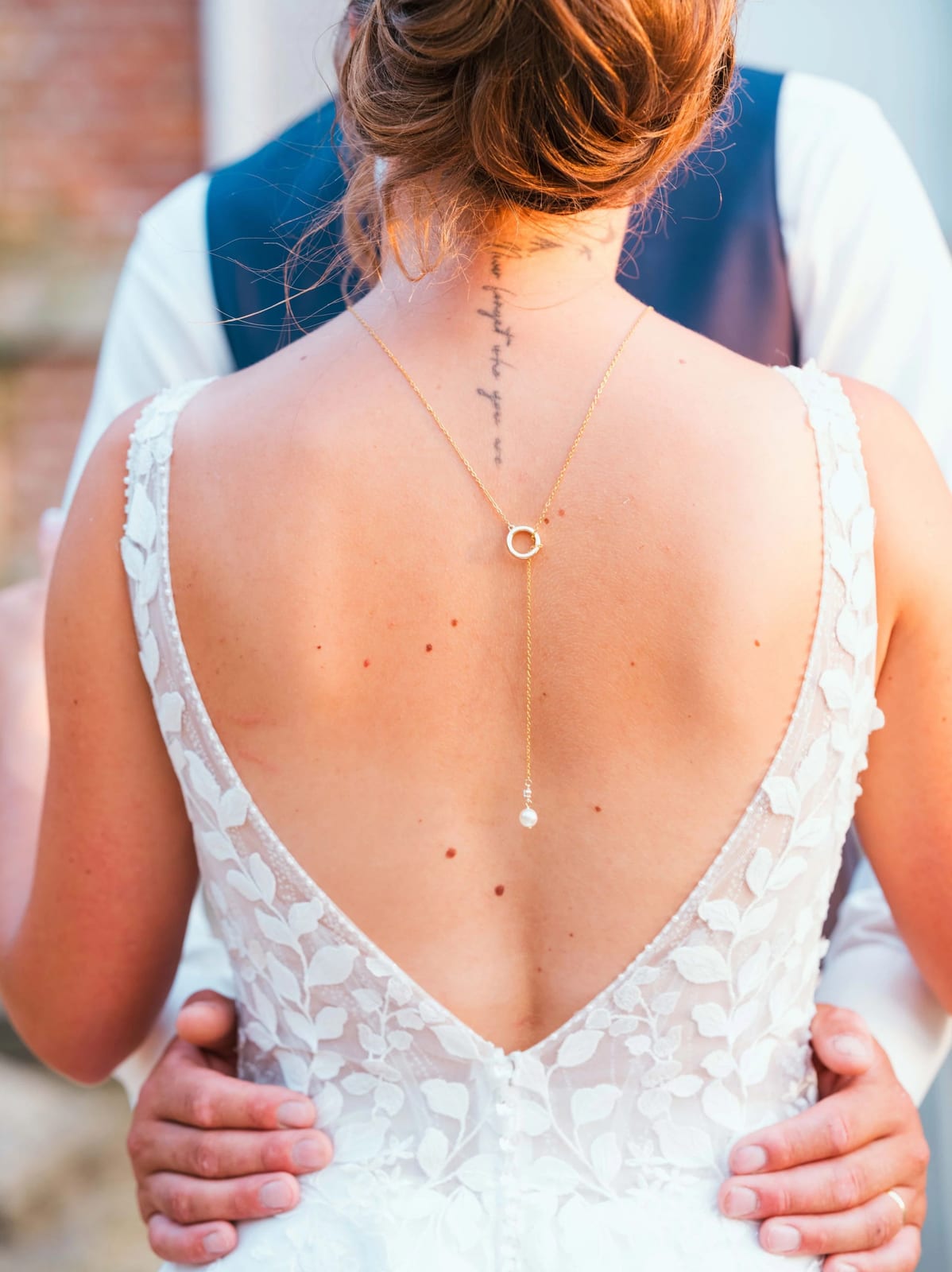Le dos entièrement ouvert de la robe d'Amélie dans la lumière dorée, chignon et collier, mariage au Les Voûtes du Plessier, par Jean-Baptiste Argyre (Jaysphotography)