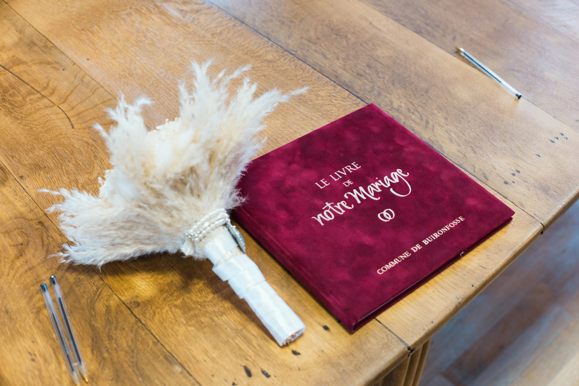 Le livre d'or bordeaux et le bouquet de pampa posés sur la table, mariage au Buironfosse (Aisne), par Jean-Baptiste Argyre (Jaysphotography)