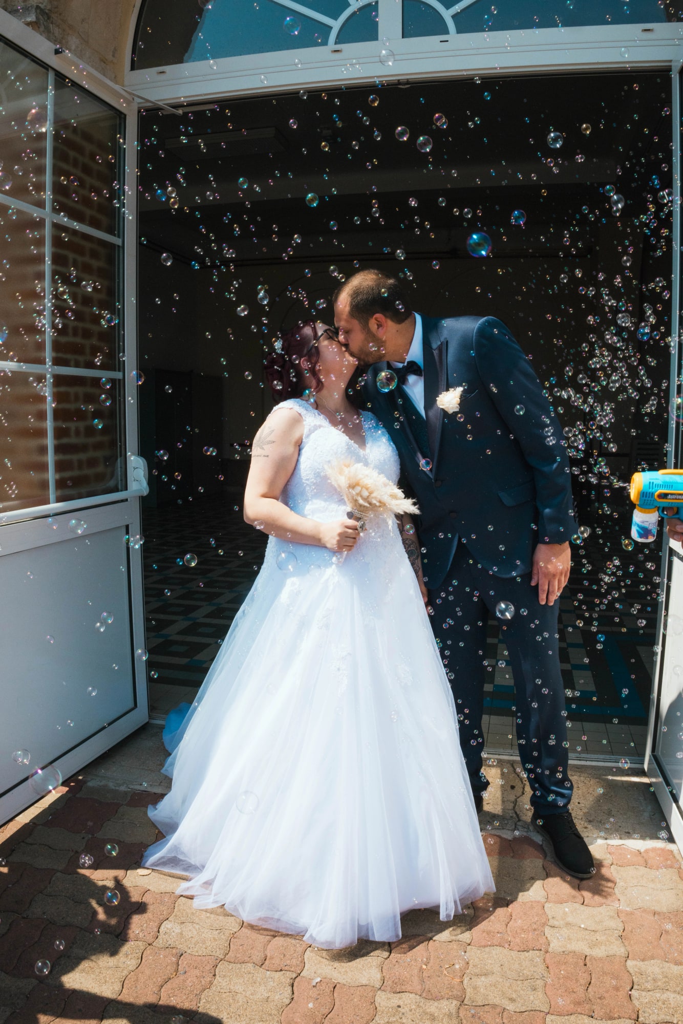 Angélique et Antoine s'embrassent sous une pluie de bulles à la sortie, mariage au Buironfosse (Aisne), par Jean-Baptiste Argyre (Jaysphotography)