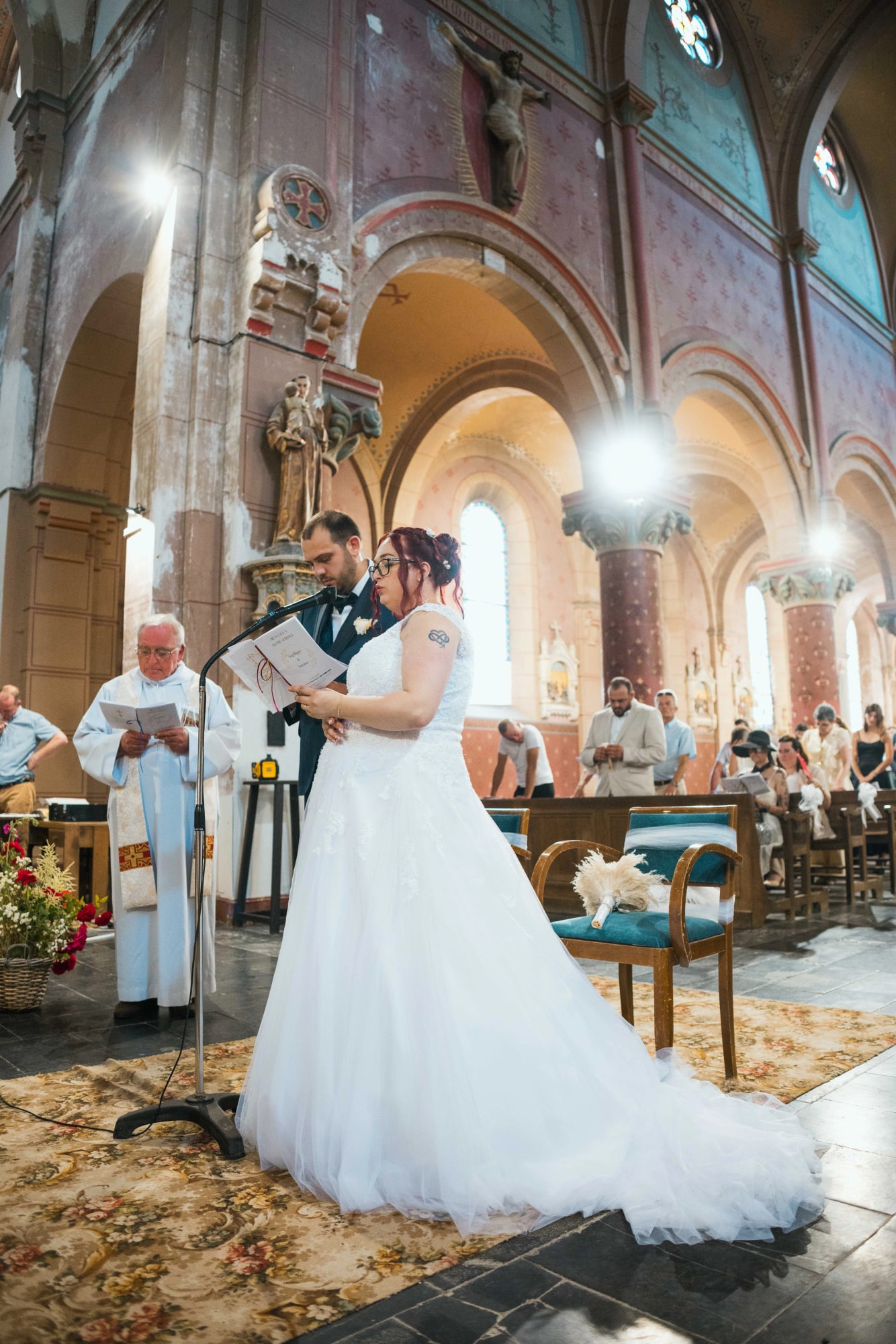 Les mariés enlacés devant le prêtre dans la nef de brique de l'église, mariage au Buironfosse (Aisne), par Jean-Baptiste Argyre (Jaysphotography)