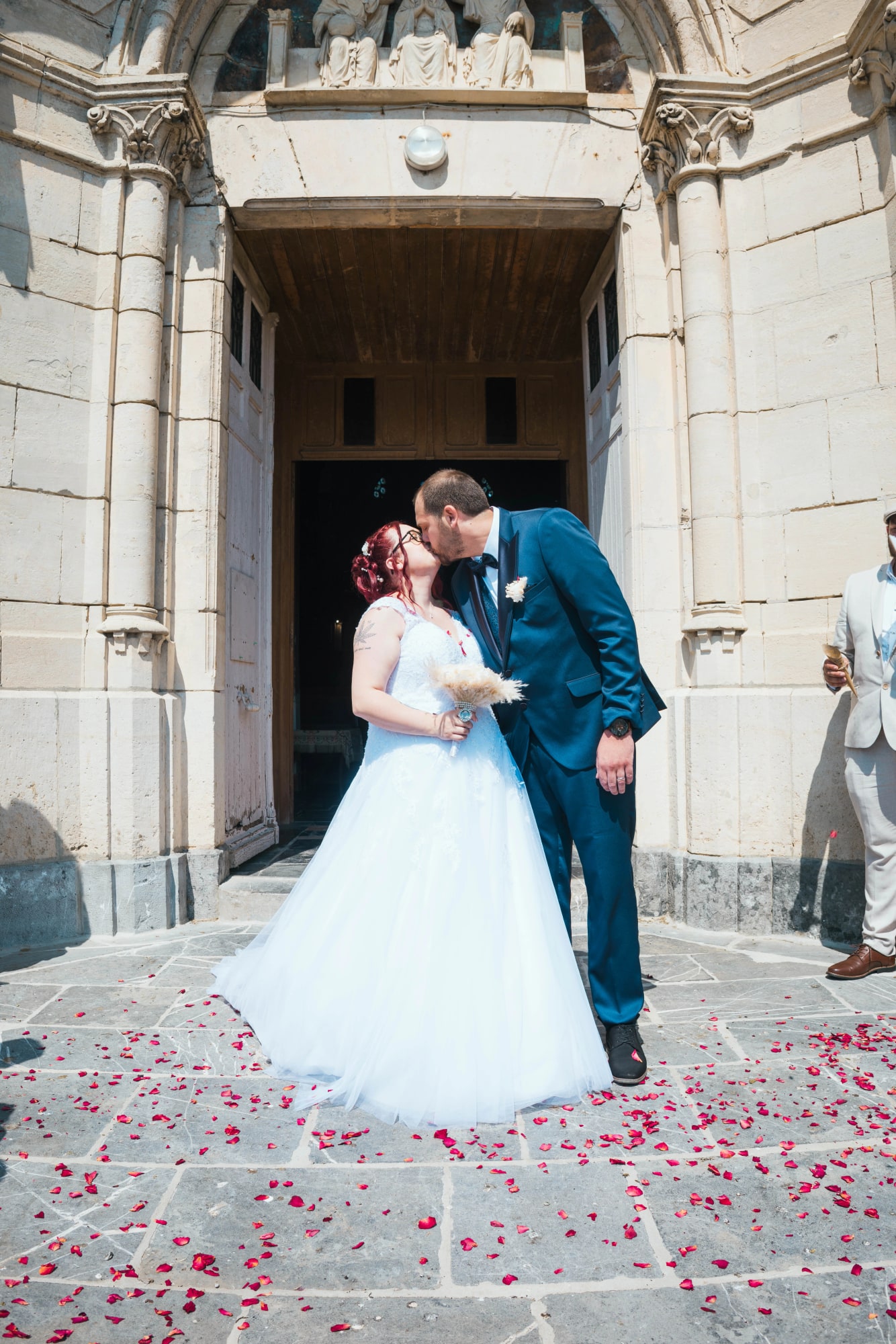 Le baiser des mariés sur le parvis de l'église, tapis de pétales de roses au sol, mariage au Buironfosse (Aisne), par Jean-Baptiste Argyre (Jaysphotography)