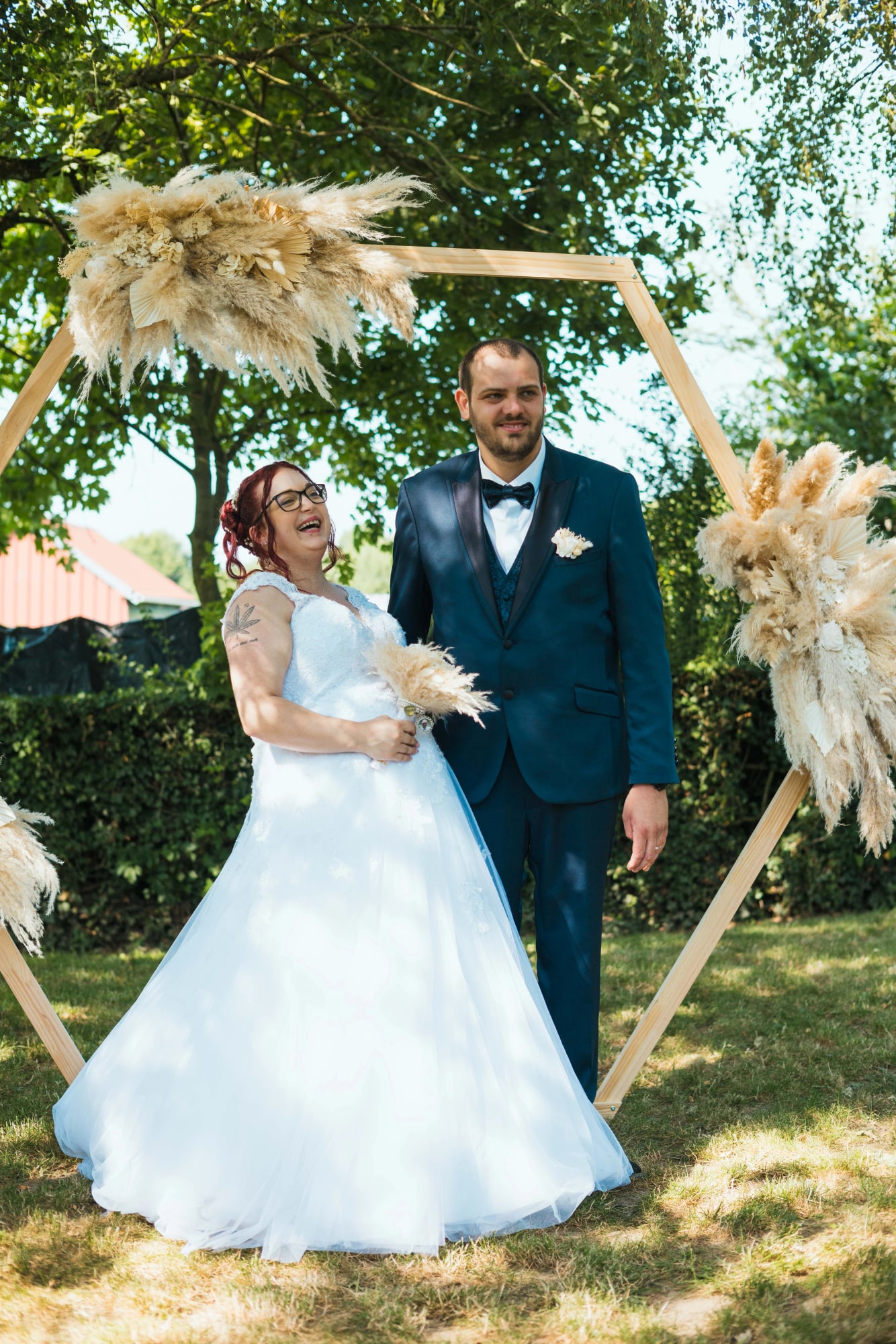 Angélique et Antoine rient sous l'arche hexagonale en pampa de leur cérémonie, mariage au Buironfosse (Aisne), par Jean-Baptiste Argyre (Jaysphotography)