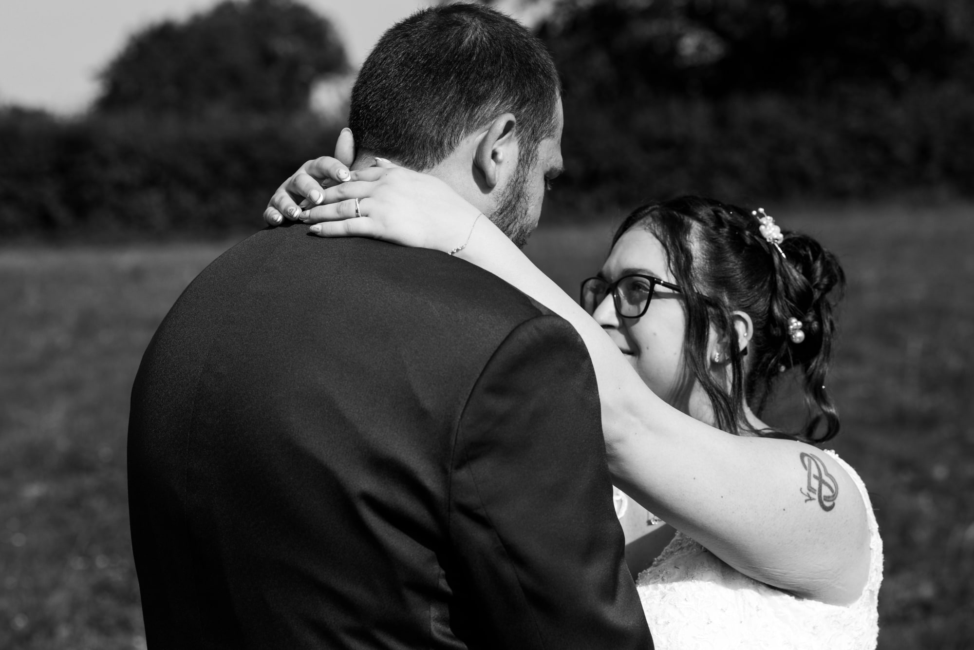 Portrait en noir et blanc des mariés enlacés dans la prairie, Angélique les bras autour du cou d'Antoine, mariage au Buironfosse (Aisne), par Jean-Baptiste Argyre (Jaysphotography)