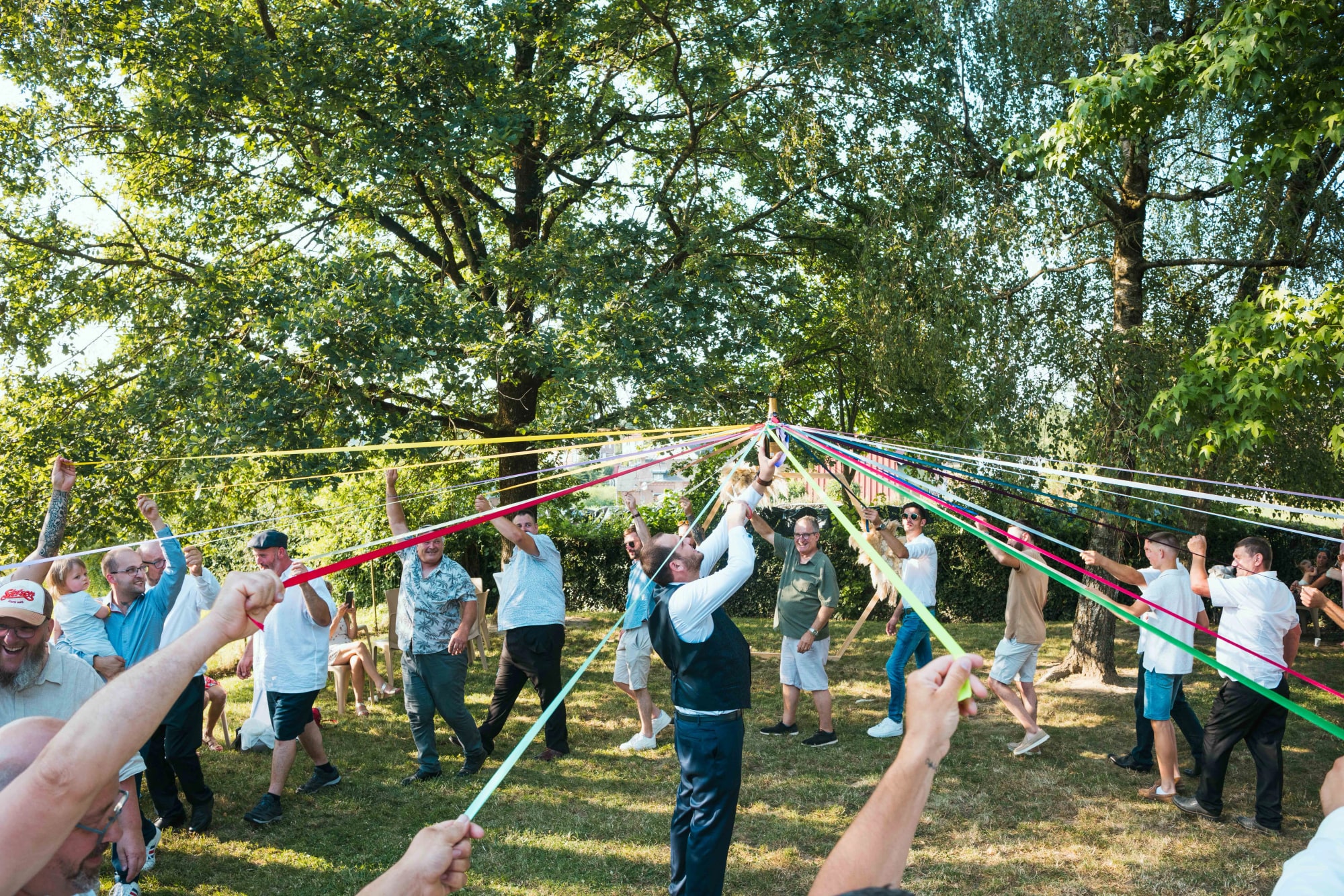 La ronde des rubans autour de la bouteille au vin d'honneur, invités et rubans multicolores tendus, mariage au Buironfosse (Aisne), par Jean-Baptiste Argyre (Jaysphotography)