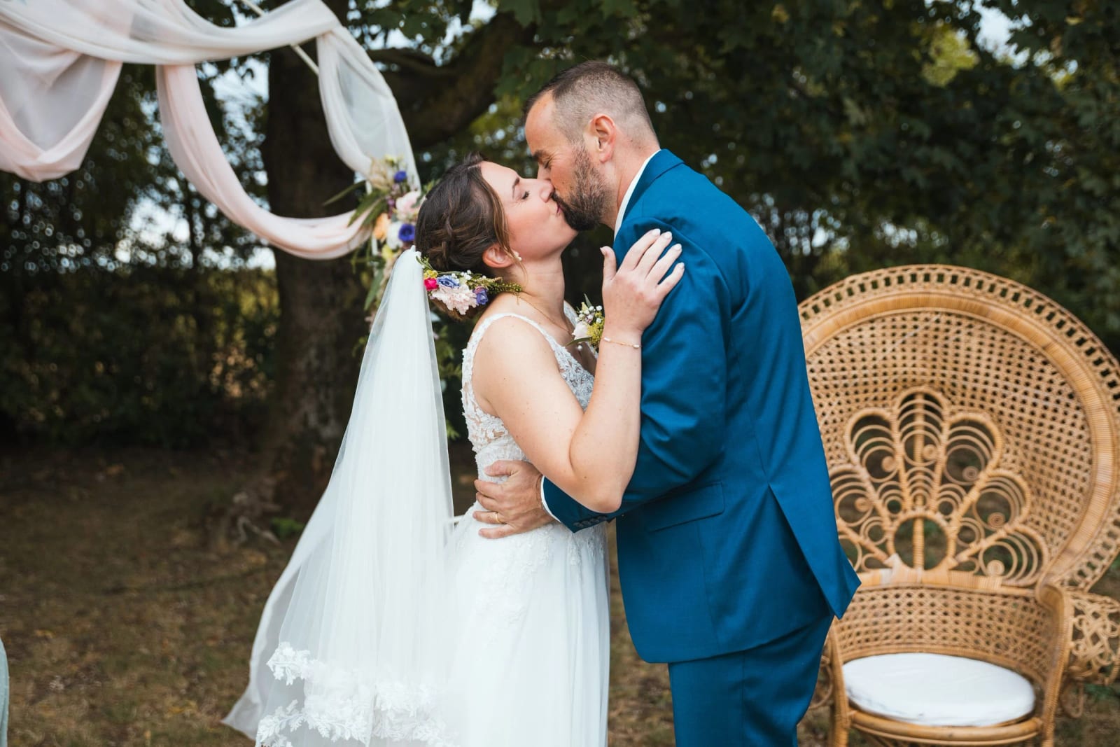 Les mariés s'embrassent pendant la cérémonie laïque dans le jardin de La Mézandrée, fauteuil de rotin et décor champêtre, mariage au La Mézandrée, par Jean-Baptiste Argyre (Jaysphotography)