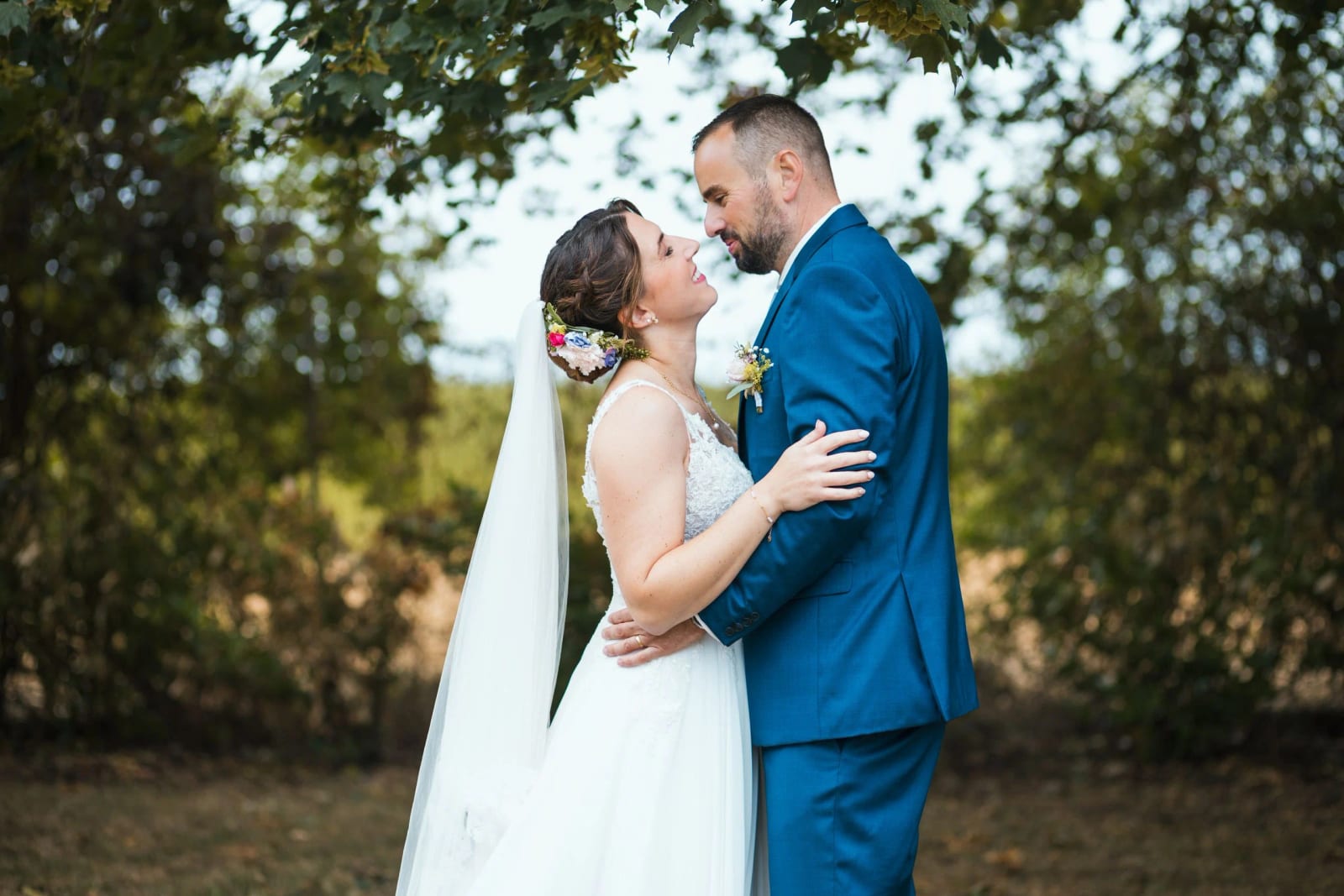 Les mariés enlacés sous les arbres en fin de journée, costume bleu et robe blanche, La Mézandrée, mariage au La Mézandrée, par Jean-Baptiste Argyre (Jaysphotography)