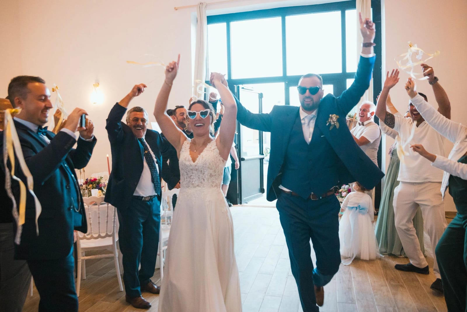 Entrée en salle des mariés sous les poutres de la grange, les invités lèvent les bras, La Mézandrée, mariage au La Mézandrée, par Jean-Baptiste Argyre (Jaysphotography)