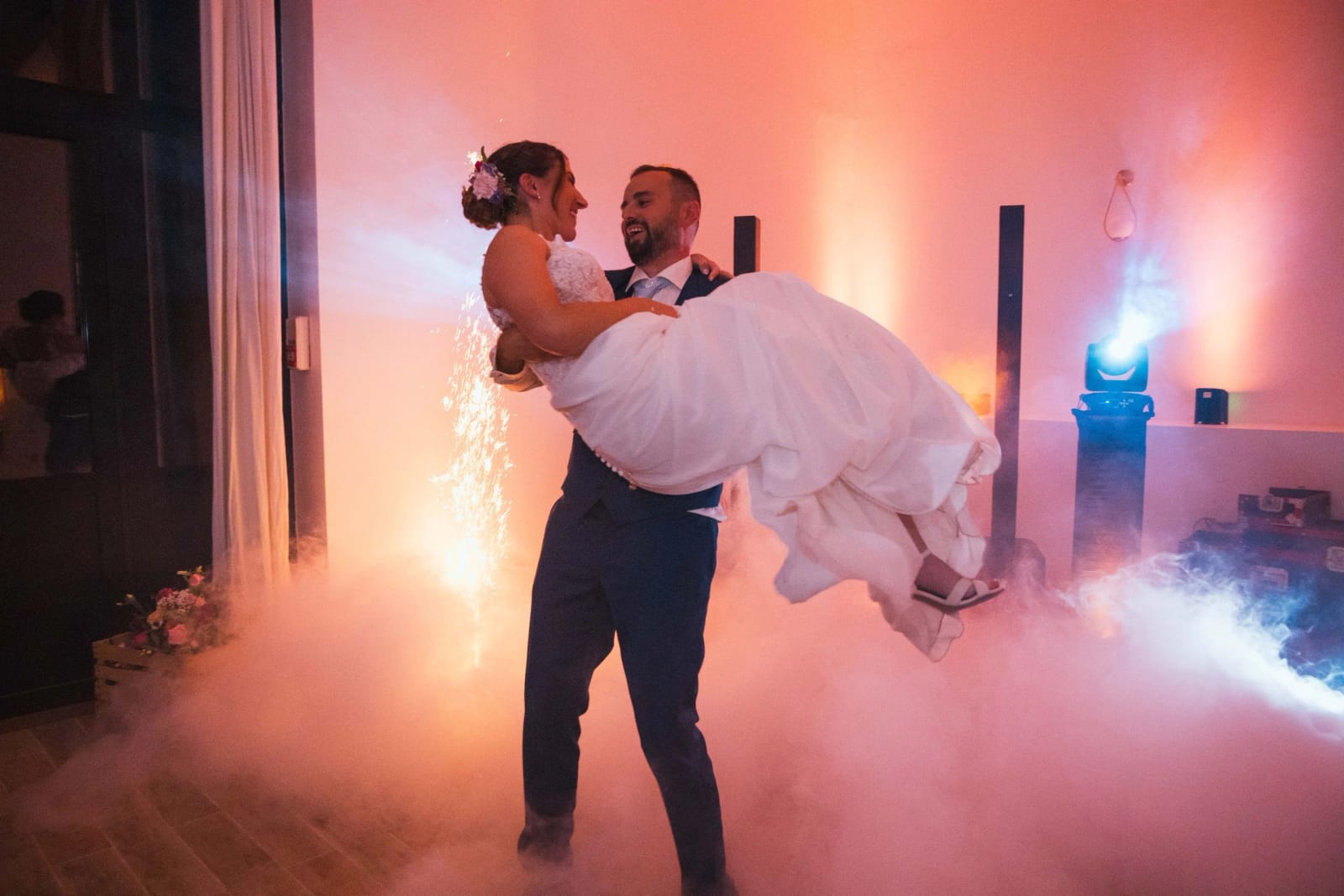 Ouverture de bal : le marié soulève la mariée dans une fumée éclairée en rose devant une fontaine à étincelles, mariage au La Mézandrée, par Jean-Baptiste Argyre (Jaysphotography)
