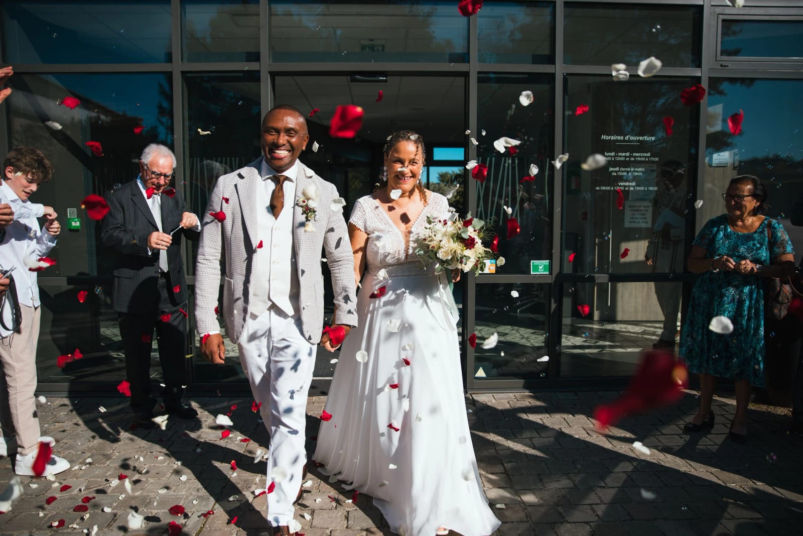 Sortie de la mairie d'Auneuil sous une pluie de pétales de roses rouges et blanches, façade vitrée, mariage au Château de la Houssoye, par Jean-Baptiste Argyre (Jaysphotography)