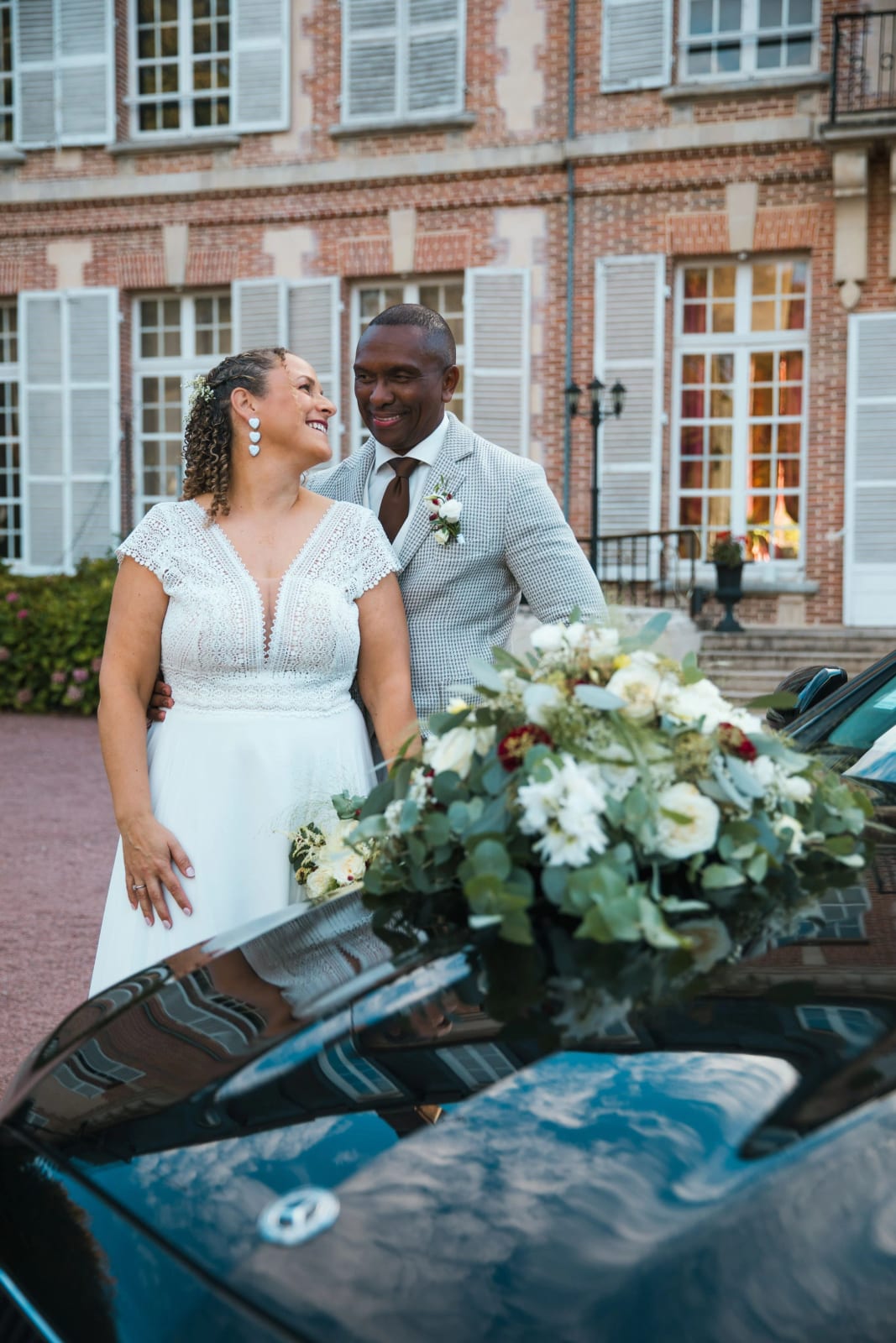 Les mariés devant la façade du Château de la Houssoye, bouquet de roses blanches sur le capot de la Mercedes au premier plan, mariage au Château de la Houssoye, par Jean-Baptiste Argyre (Jaysphotography)