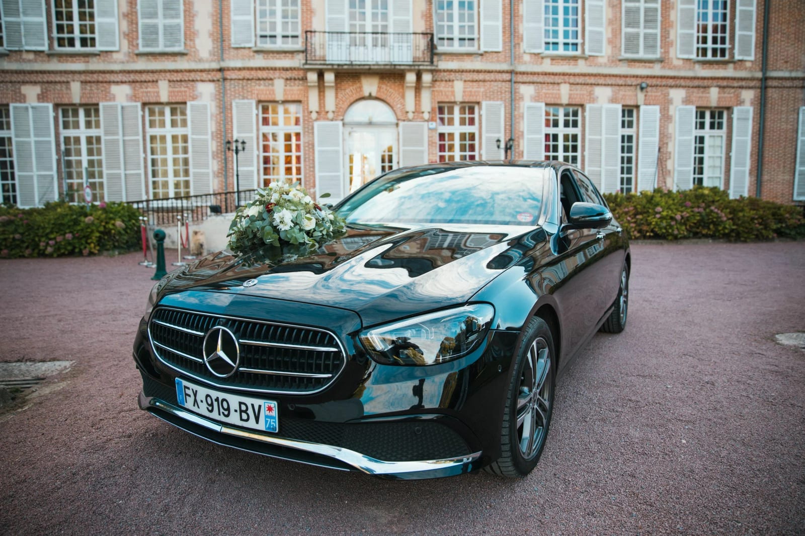 Mercedes noire décorée d'un bouquet blanc dans la cour de gravier rose du Château de la Houssoye, mariage au Château de la Houssoye, par Jean-Baptiste Argyre (Jaysphotography)