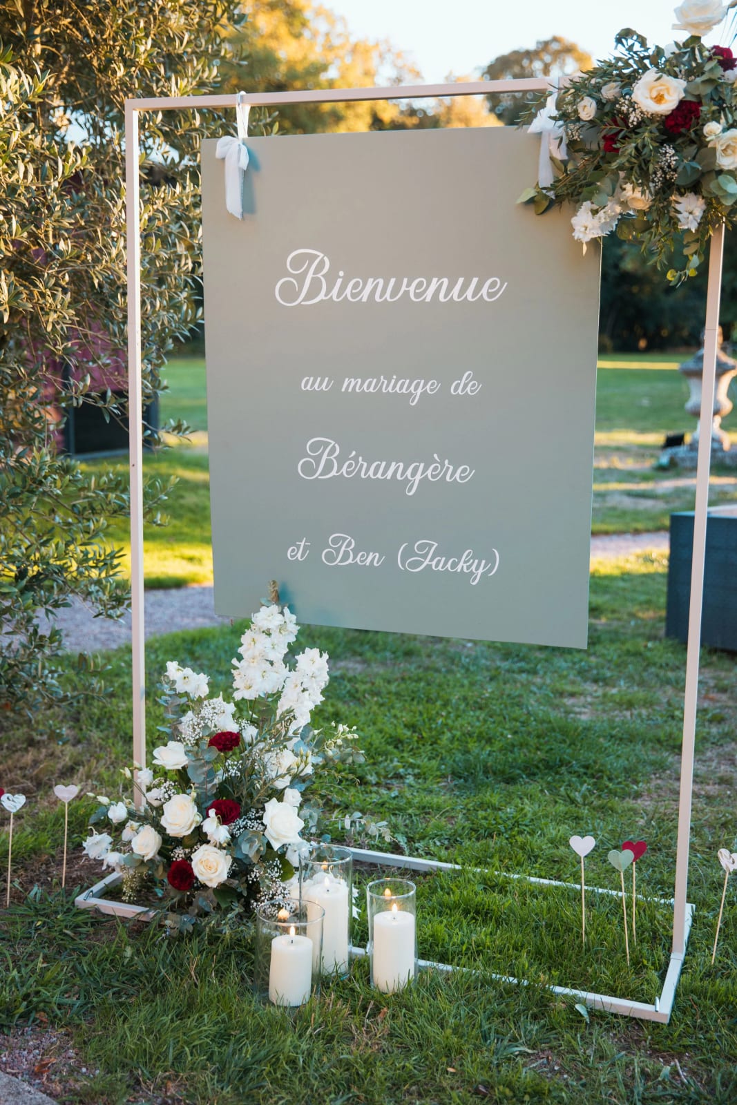 Panneau d'accueil vert sauge « Bienvenue au mariage de Bérangère et Ben (Jacky) » sur cadre blanc dans le parc, fleurs et bougies au pied, mariage au Château de la Houssoye, par Jean-Baptiste Argyre (Jaysphotography)