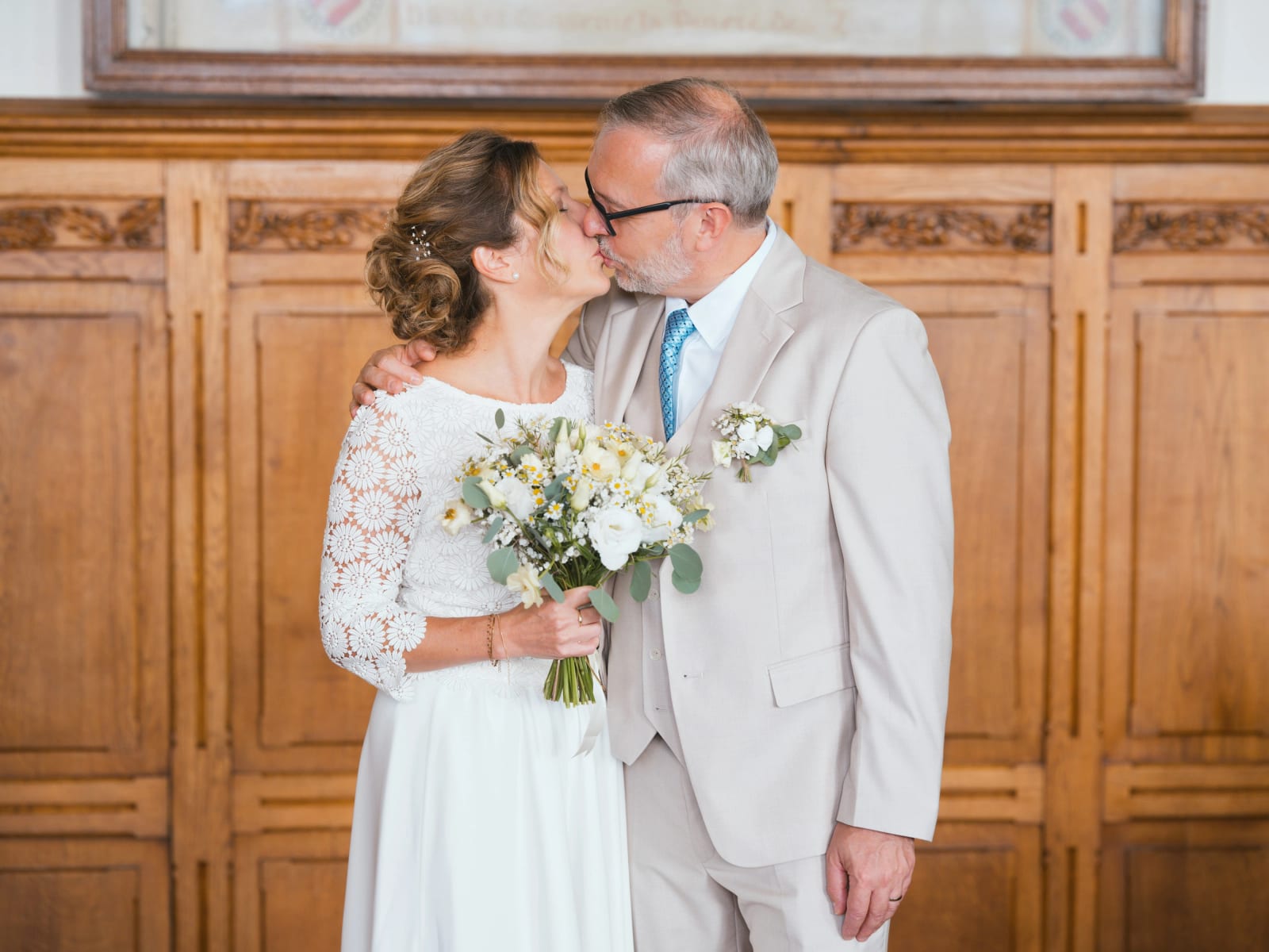 Premier baiser des mariés devant les boiseries sculptées de la salle des mariages, bouquet de roses blanches et marguerites, mariage à la Mairie de Senlis, par Jean-Baptiste Argyre (Jaysphotography)