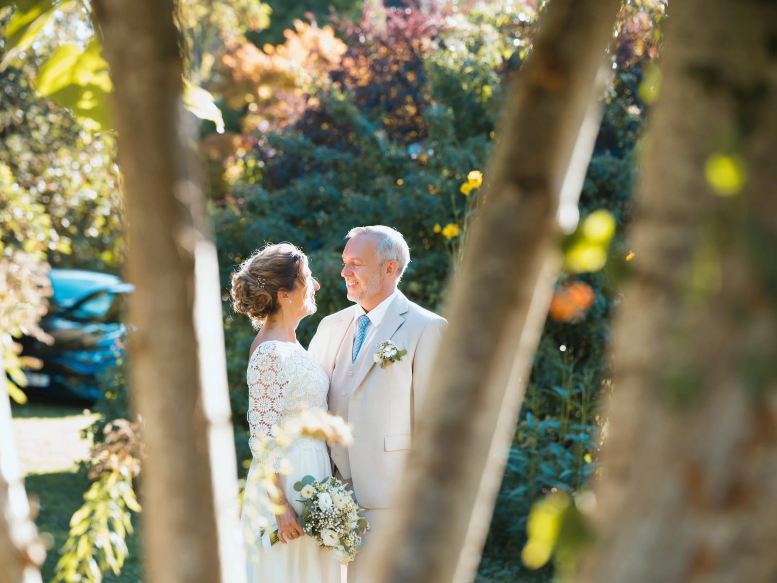 Les mariés face à face dans un jardin fleuri, photographiés entre deux troncs d'arbre, mariage à la Mairie de Senlis, par Jean-Baptiste Argyre (Jaysphotography)