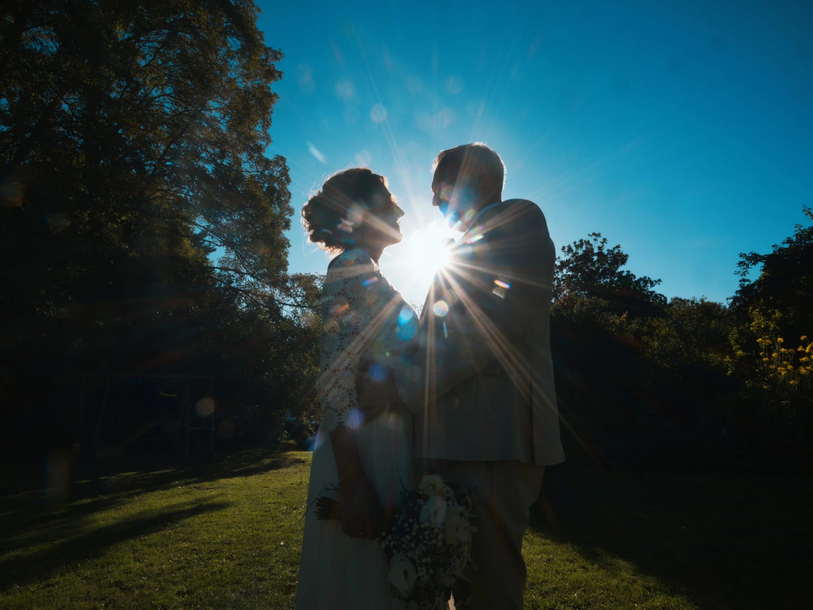 Silhouettes des mariés sur une pelouse, le soleil en étoile entre leurs visages, ciel bleu, mariage à la Mairie de Senlis, par Jean-Baptiste Argyre (Jaysphotography)