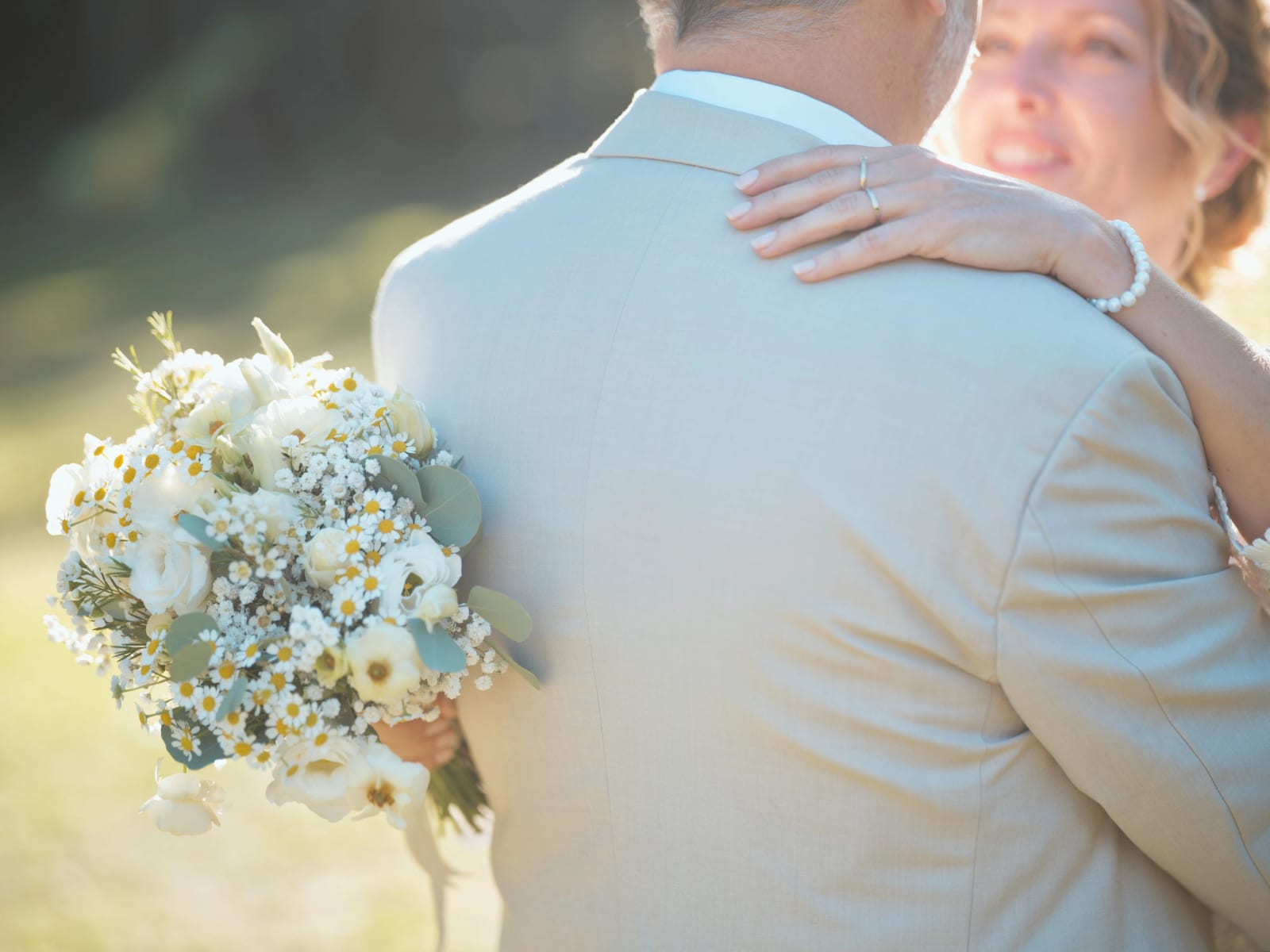 Le bouquet de roses blanches et marguerites tenu dans le dos du marié, la main de la mariée et son alliance sur son épaule, mariage à la Mairie de Senlis, par Jean-Baptiste Argyre (Jaysphotography)