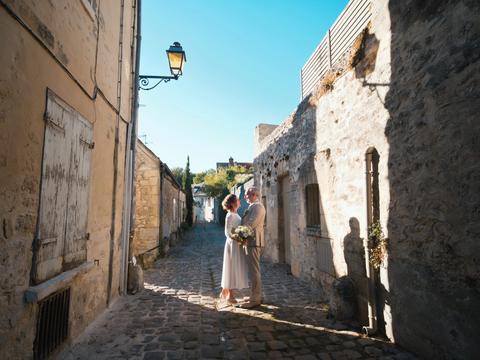 Les mariés dans une ruelle pavée du vieux Senlis entre des murs de pierre, lanterne en fer forgé, mariage à la Mairie de Senlis, par Jean-Baptiste Argyre (Jaysphotography)