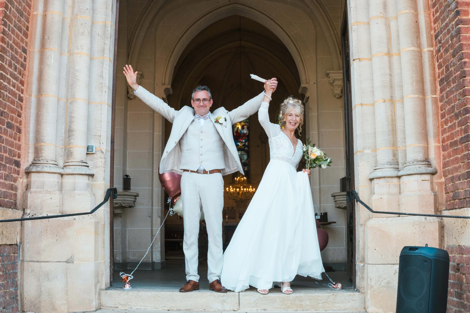 Les mariés bras levés sous le porche de l'église, à la sortie de la cérémonie, mariage au Valescourt (Oise), par Jean-Baptiste Argyre (Jaysphotography)