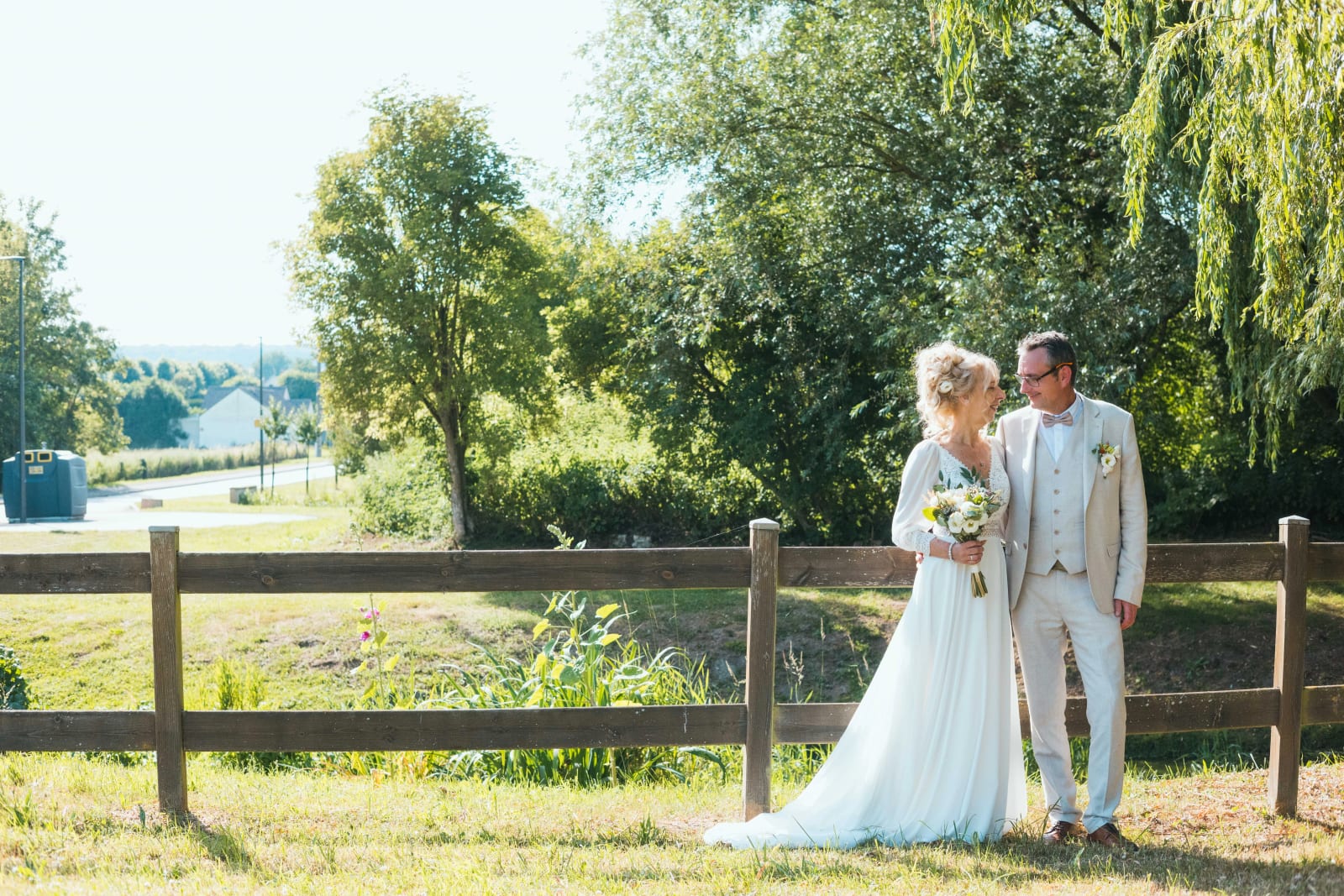 Les mariés marchant dans la prairie au bord du chemin, saules en arrière-plan, mariage au Valescourt (Oise), par Jean-Baptiste Argyre (Jaysphotography)