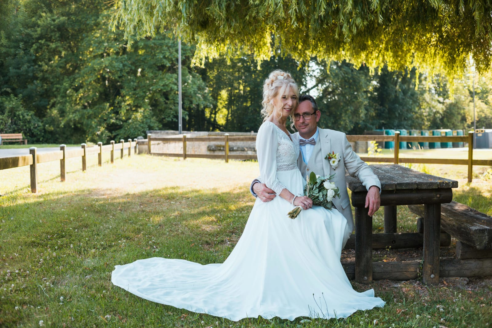 Corinne assise près d'Olivier sous le saule, traîne de la robe déployée, mariage au Valescourt (Oise), par Jean-Baptiste Argyre (Jaysphotography)