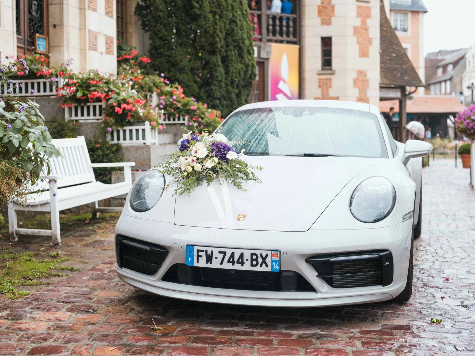 Porsche blanche des mariés ornée d'un bouquet d'hortensias violets et de roses sur le capot, pavés mouillés devant la mairie, mariage au Pavillon des Bains, Deauville, par Jean-Baptiste Argyre (Jaysphotography)