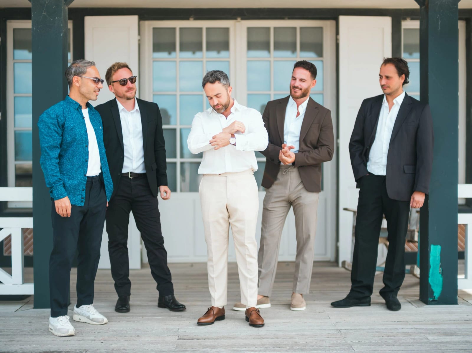 Le marié en chemise blanche et pantalon crème ajuste sa manchette, entouré de quatre amis sous un auvent de bois, mariage au Pavillon des Bains, Deauville, par Jean-Baptiste Argyre (Jaysphotography)