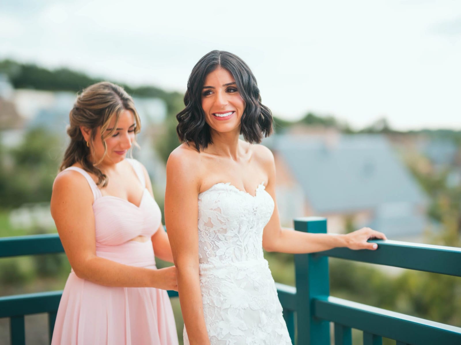 Une proche en robe rose pâle ferme la robe de la mariée sur un balcon turquoise, mariage au Pavillon des Bains, Deauville, par Jean-Baptiste Argyre (Jaysphotography)